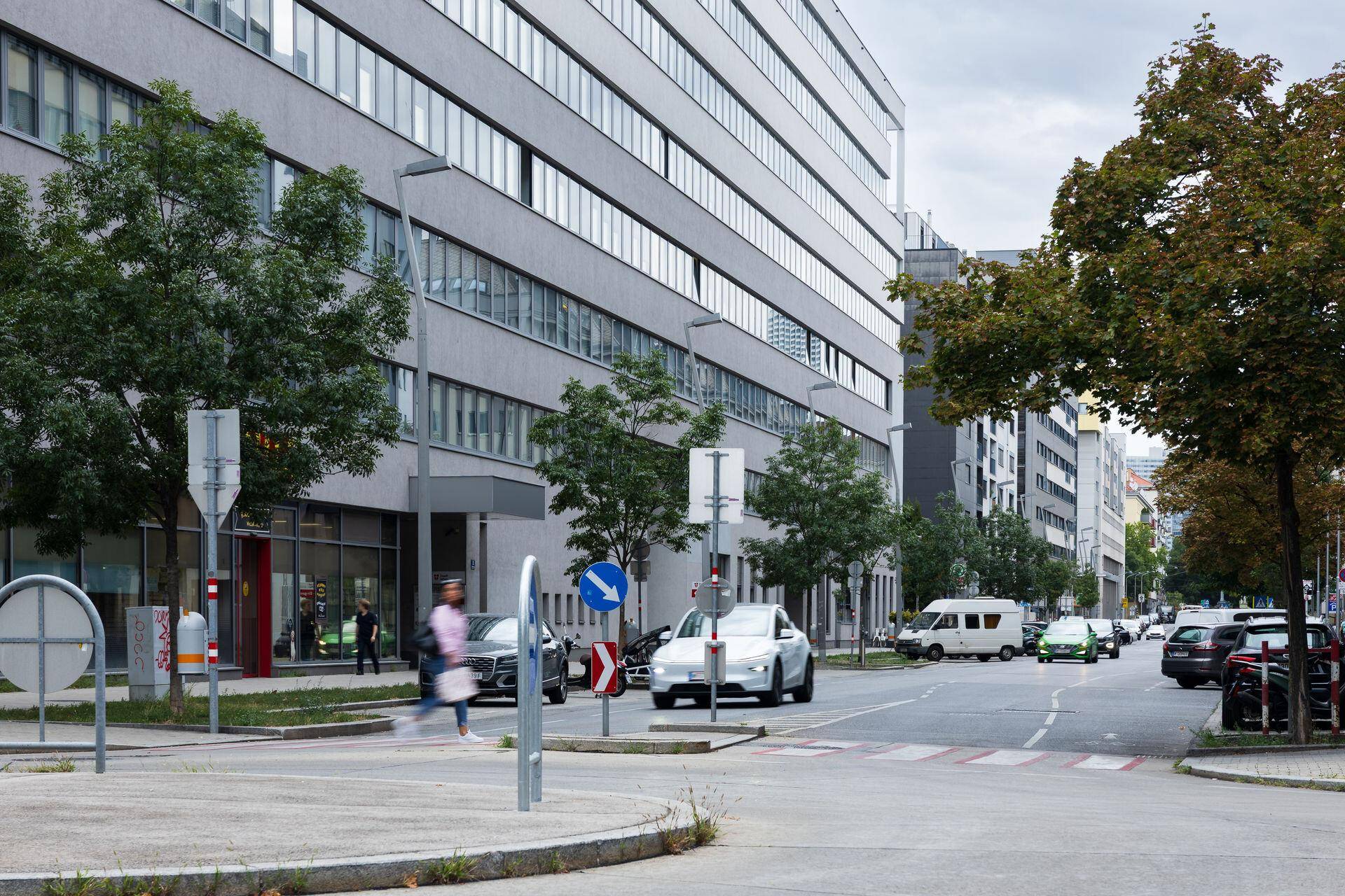 Belebtes Stadtbild mit dem modernen Gebäude im Hintergrund, Autos und Fußgängern auf der Straße.