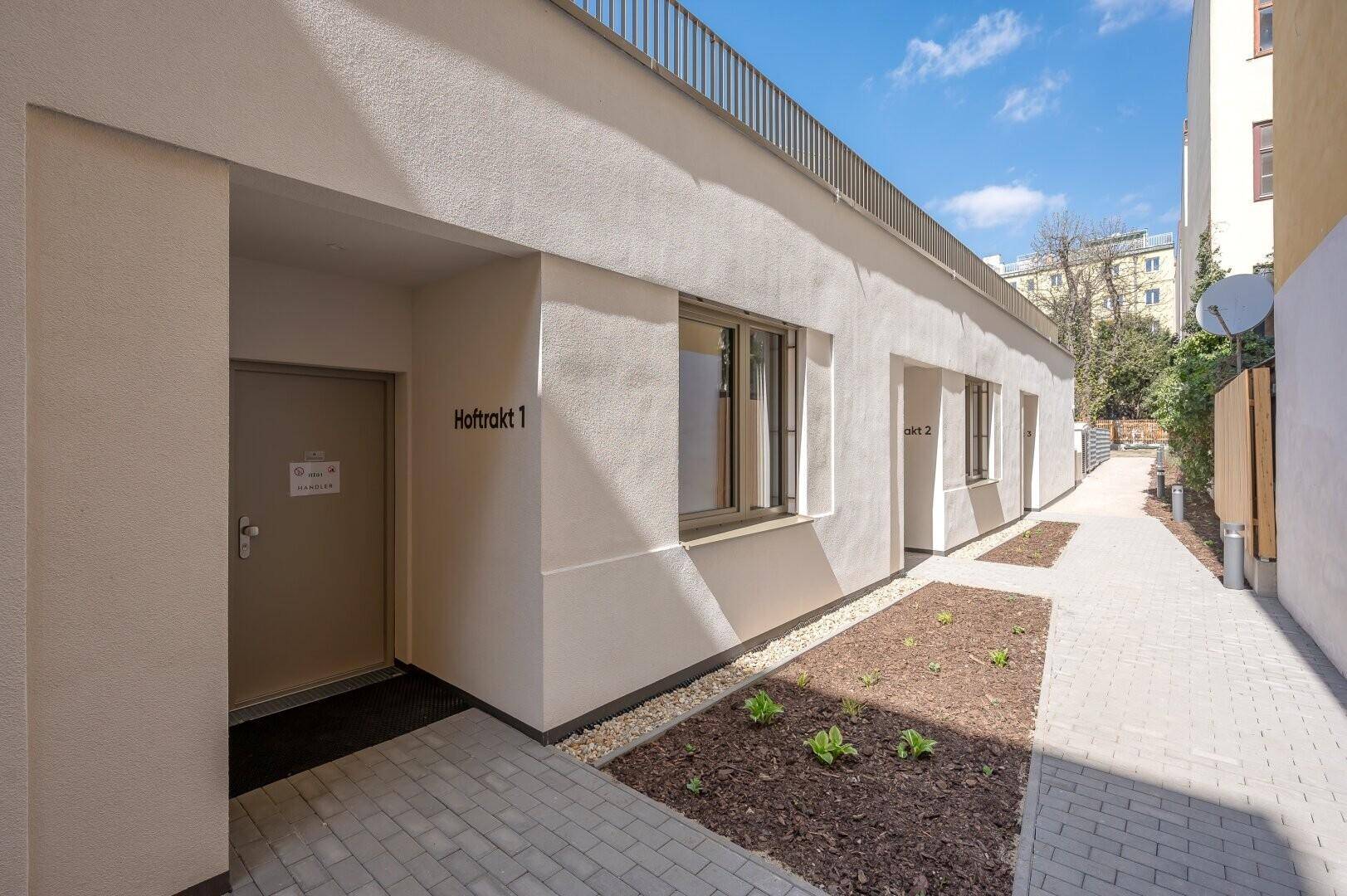 Eingangsbereich eines modernen Gebäudes mit gepflegter Außenanlage.