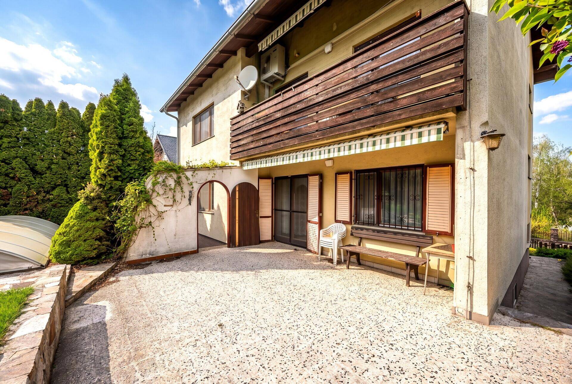 Blick auf die Terrasse und den Balkon des Hauses vom Garten aus, umgeben von viel Grün.