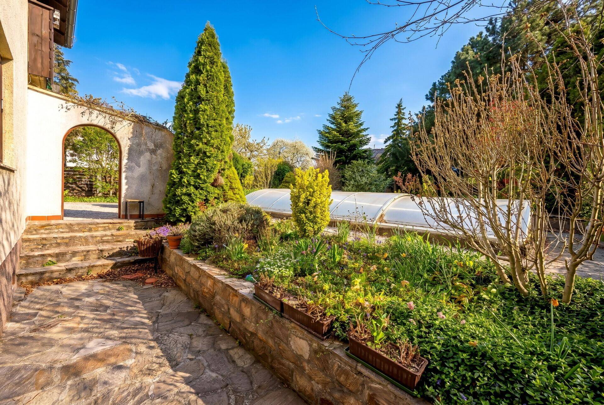 Gepflasterter Terrassenbereich mit Blumenbeeten und einem überdachten Pool im Hintergrund.