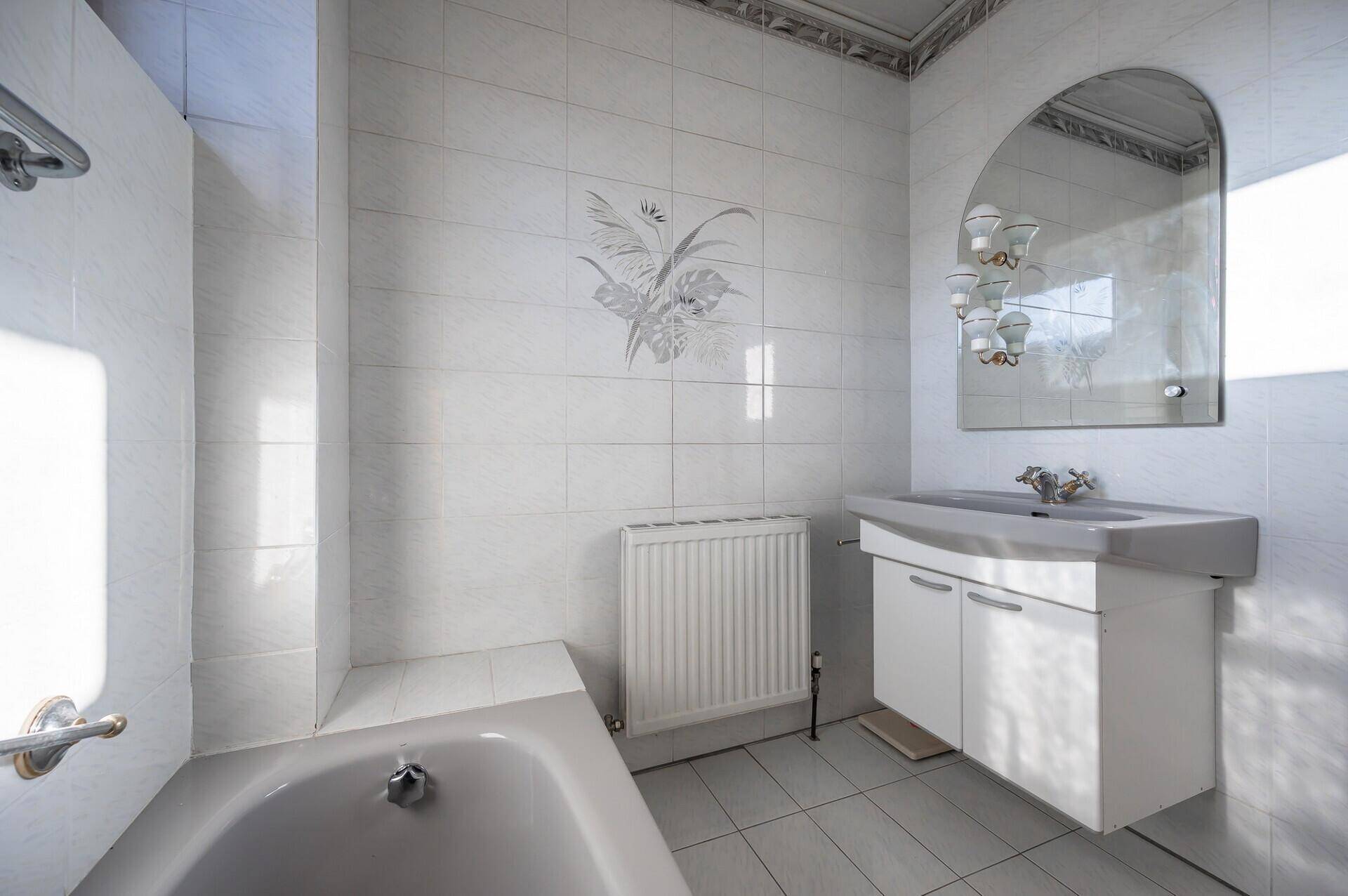 Badezimmer mit Badewanne, Waschbeckenunterschrank, Spiegel und hellen Fliesen.