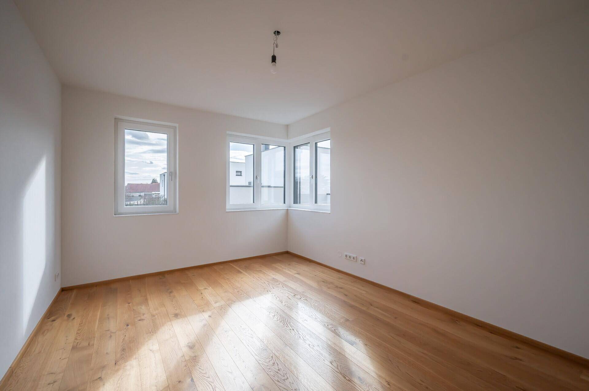 Geräumiges Schlafzimmer mit Holzboden und Eckfenstern für optimale Belichtung.