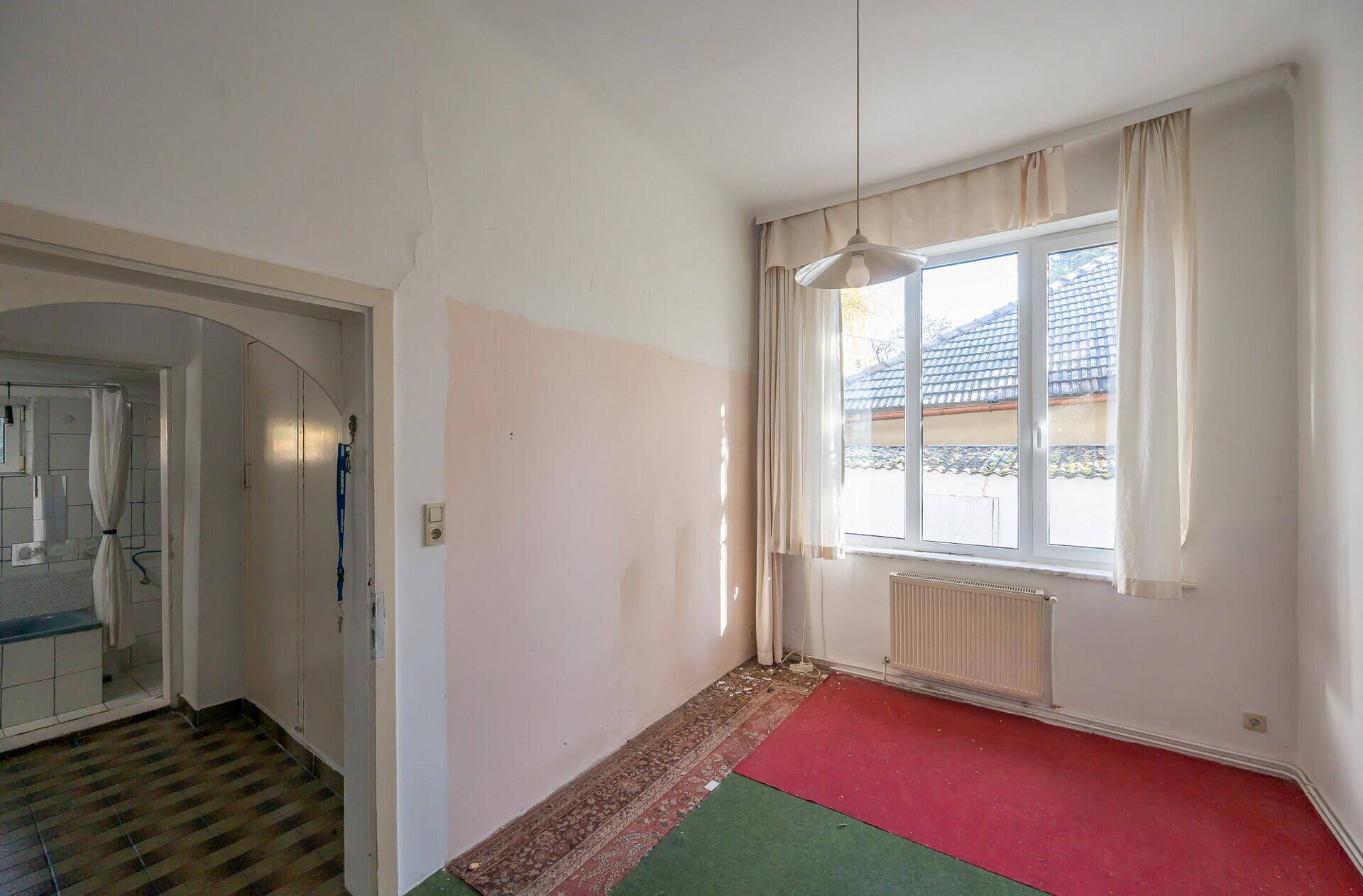 Zimmer mit Teppichboden und Fenster, das auf den Garten blickt, renovierungsbedürftig.