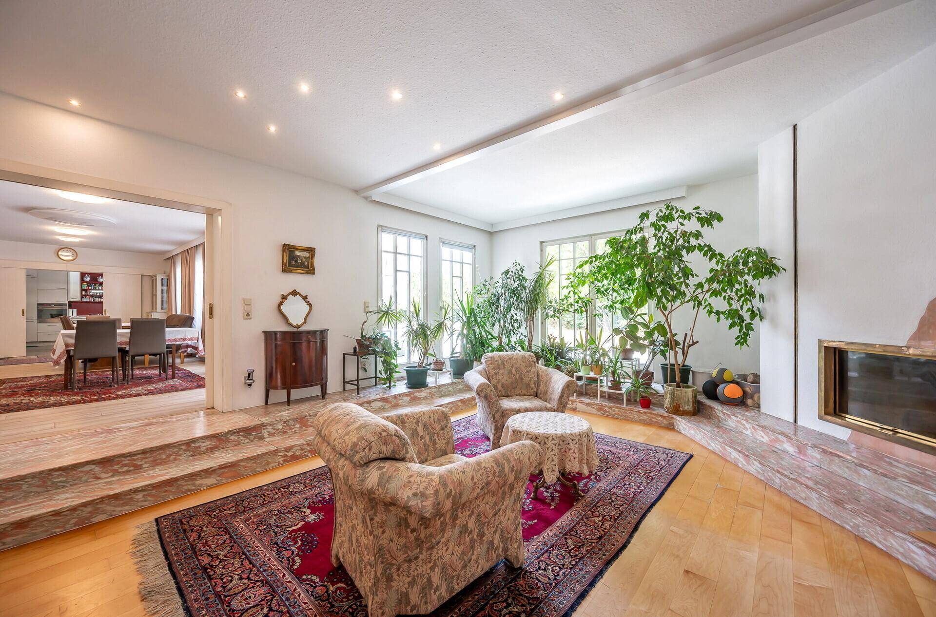 Helles Wohnzimmer mit Parkettboden, Kamin und vielen Pflanzen, offen zum Essbereich.