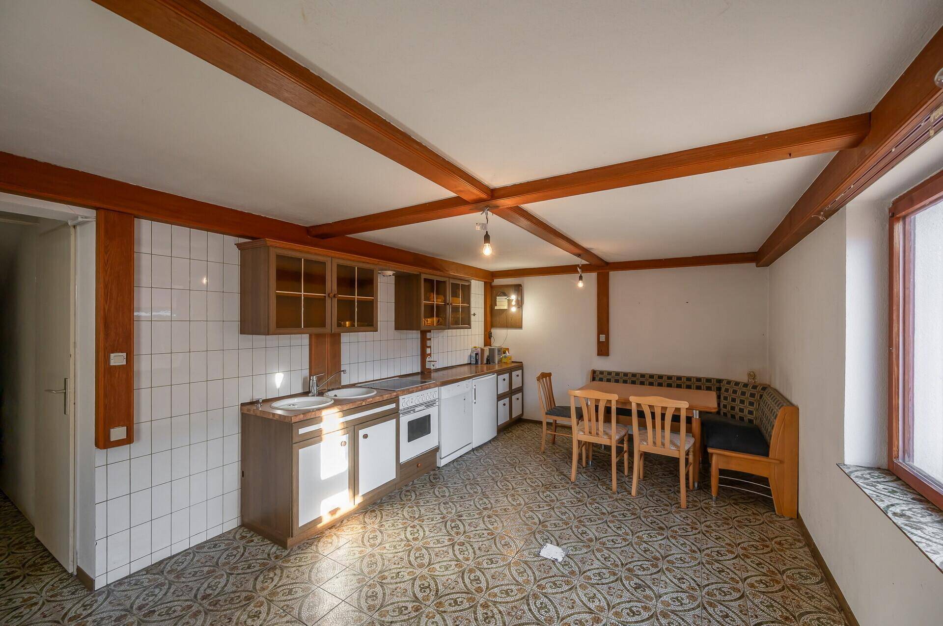 Traditionelle Wohnküche mit Holzbalken, Einbaumöbeln und Essbereich, bereit zur Modernisierung.