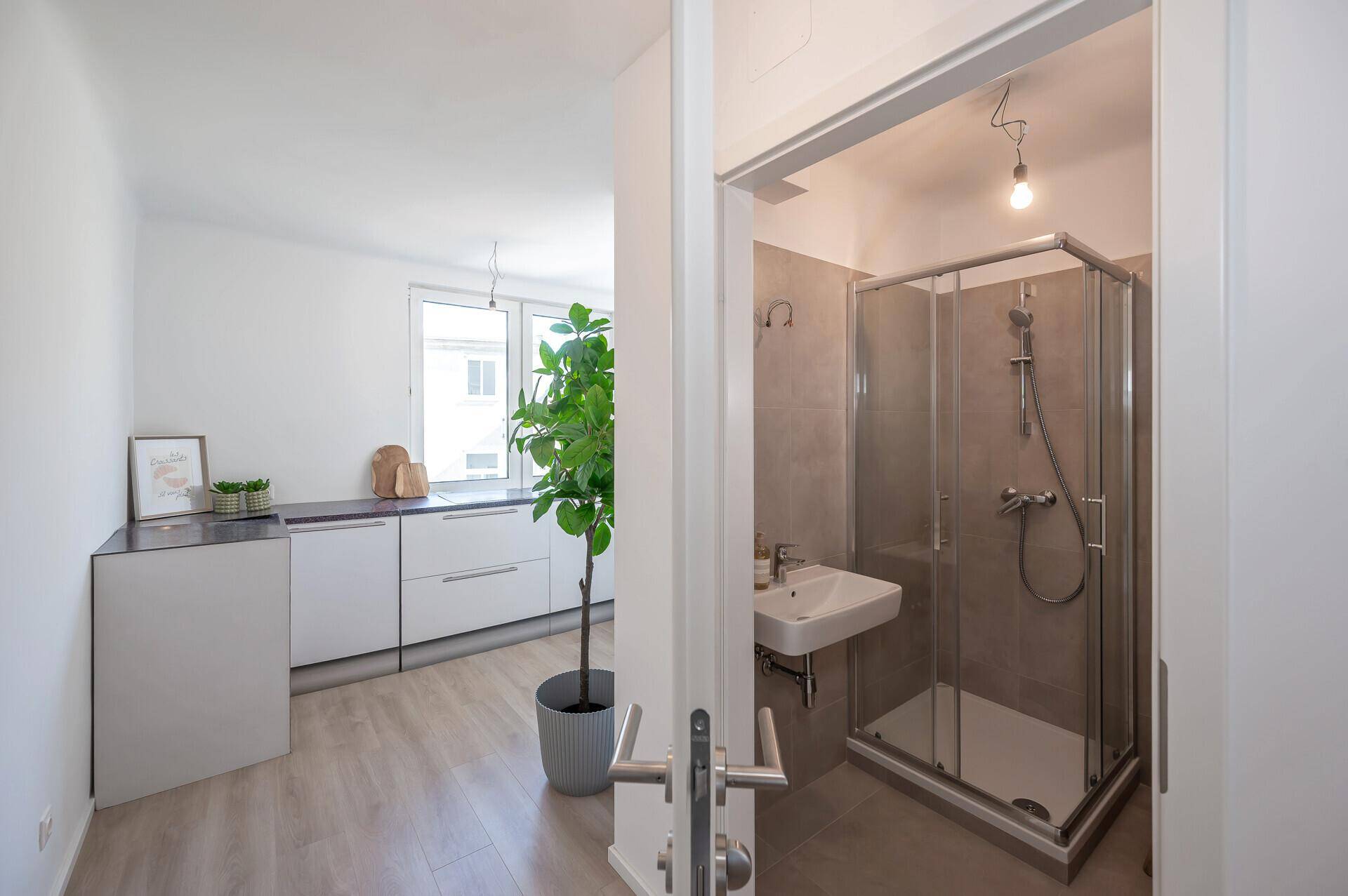 Badezimmer mit Duschkabine und Waschbecken, sichtbar vom Küchenbereich aus.