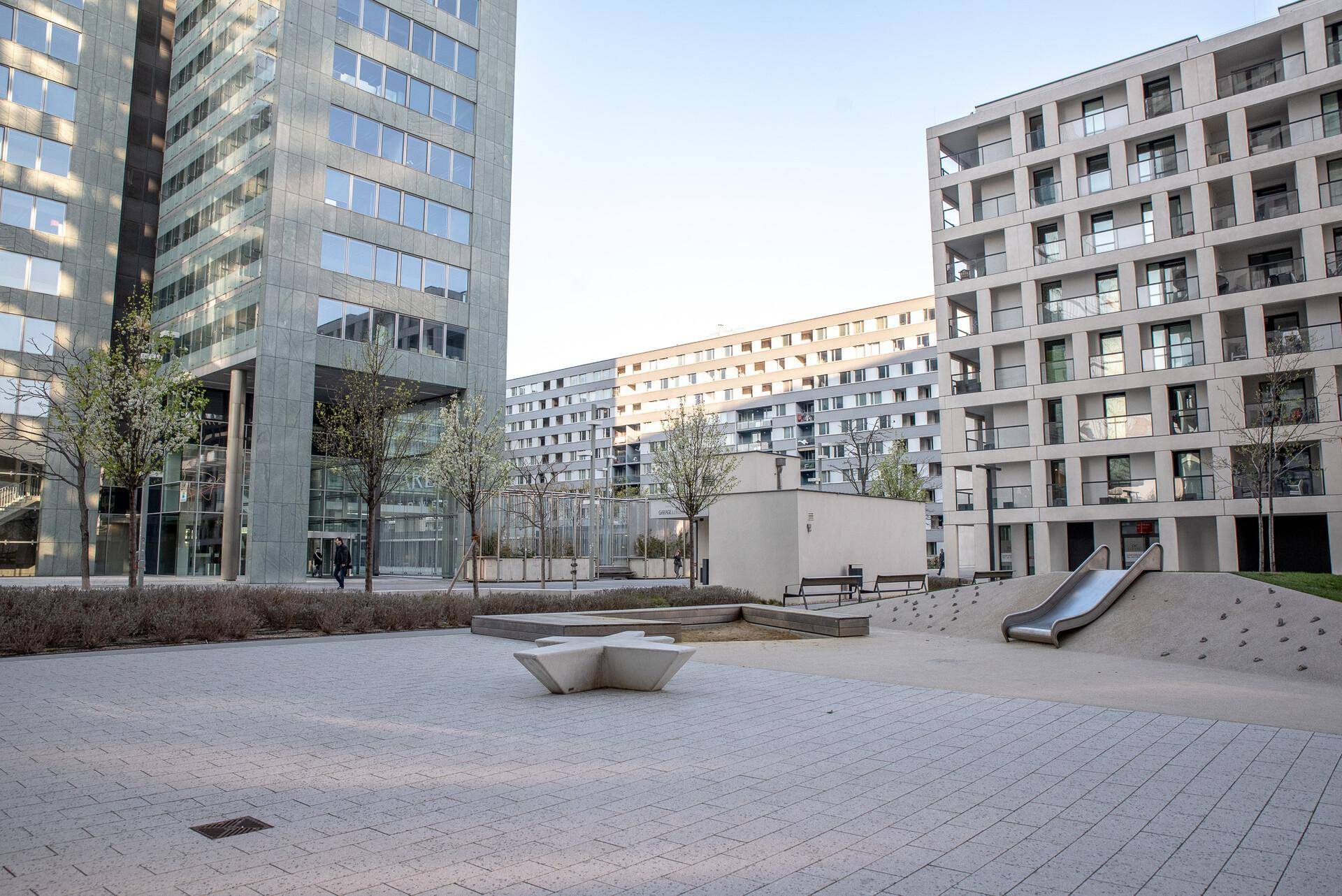 Moderne Wohnanlage mit Spielplatz und gepflasterten Wegen, umgeben von hohen Gebäuden.
