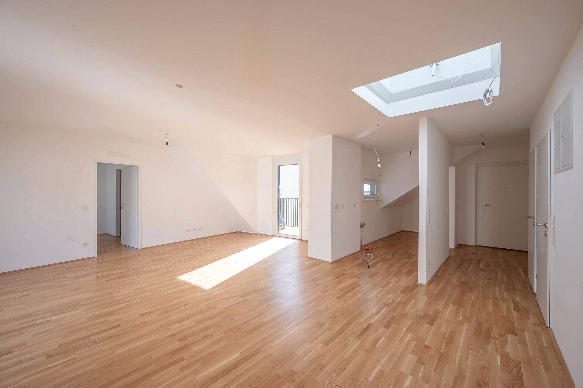 Lichtdurchfluteter Wohnbereich mit Holzparkett, großen Fenstern und einem markanten Dachfenster.
