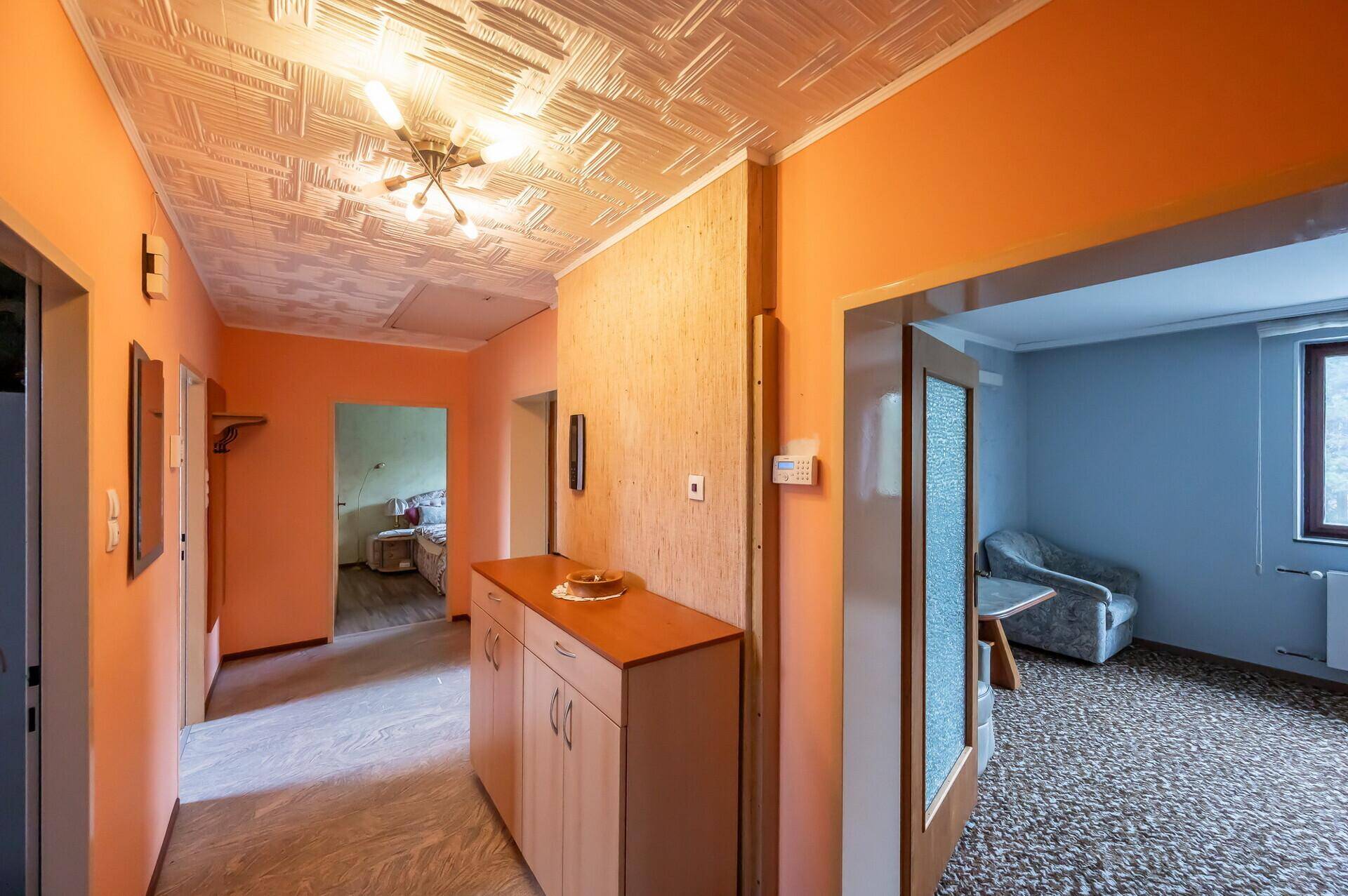 Heller Flur mit orangefarbenen Wänden, gemusterter Decke und Zugang zu angrenzenden Räumen.