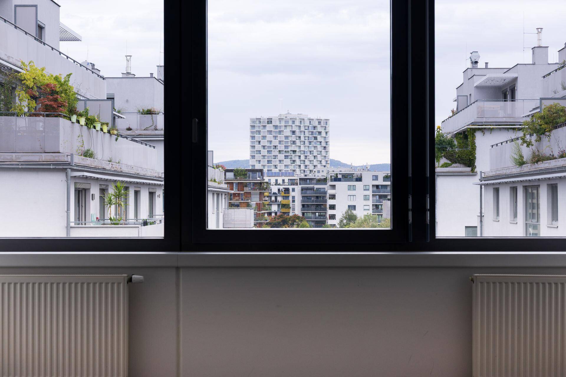 Blick aus einem Fenster auf moderne Wohngebäude mit Balkonen und einer städtischen Umgebung.