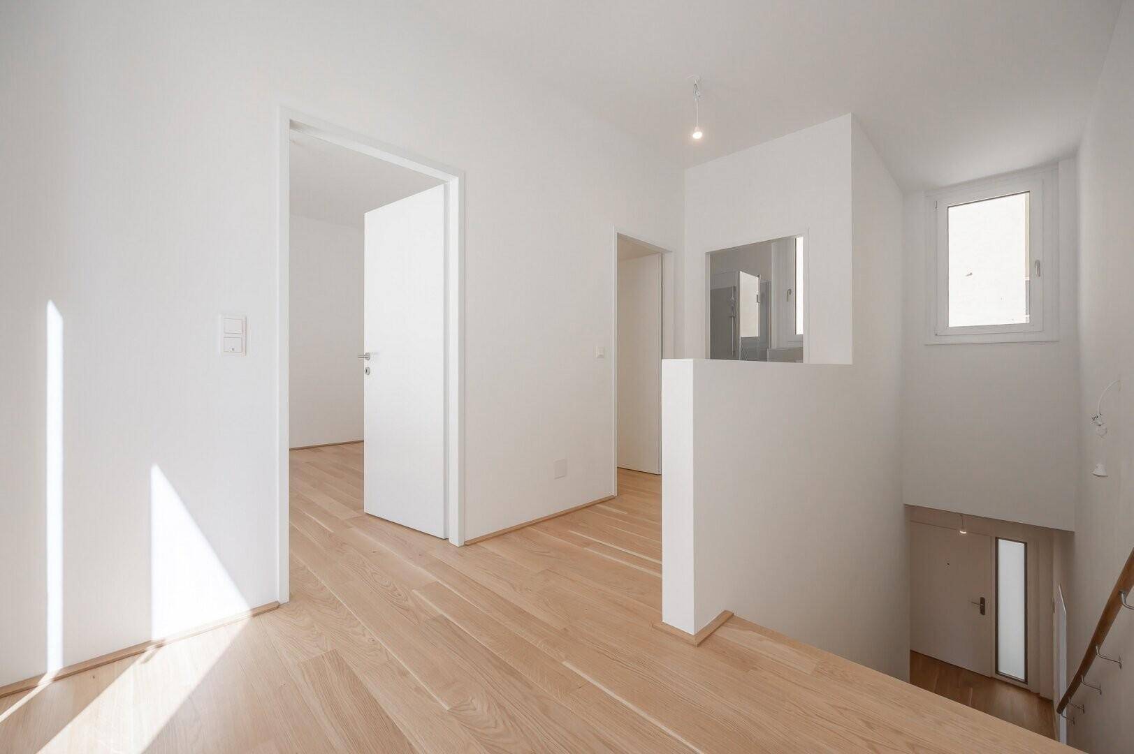 Heller Flur mit Holztreppe und natürlichem Lichteinfall durch ein Fenster.