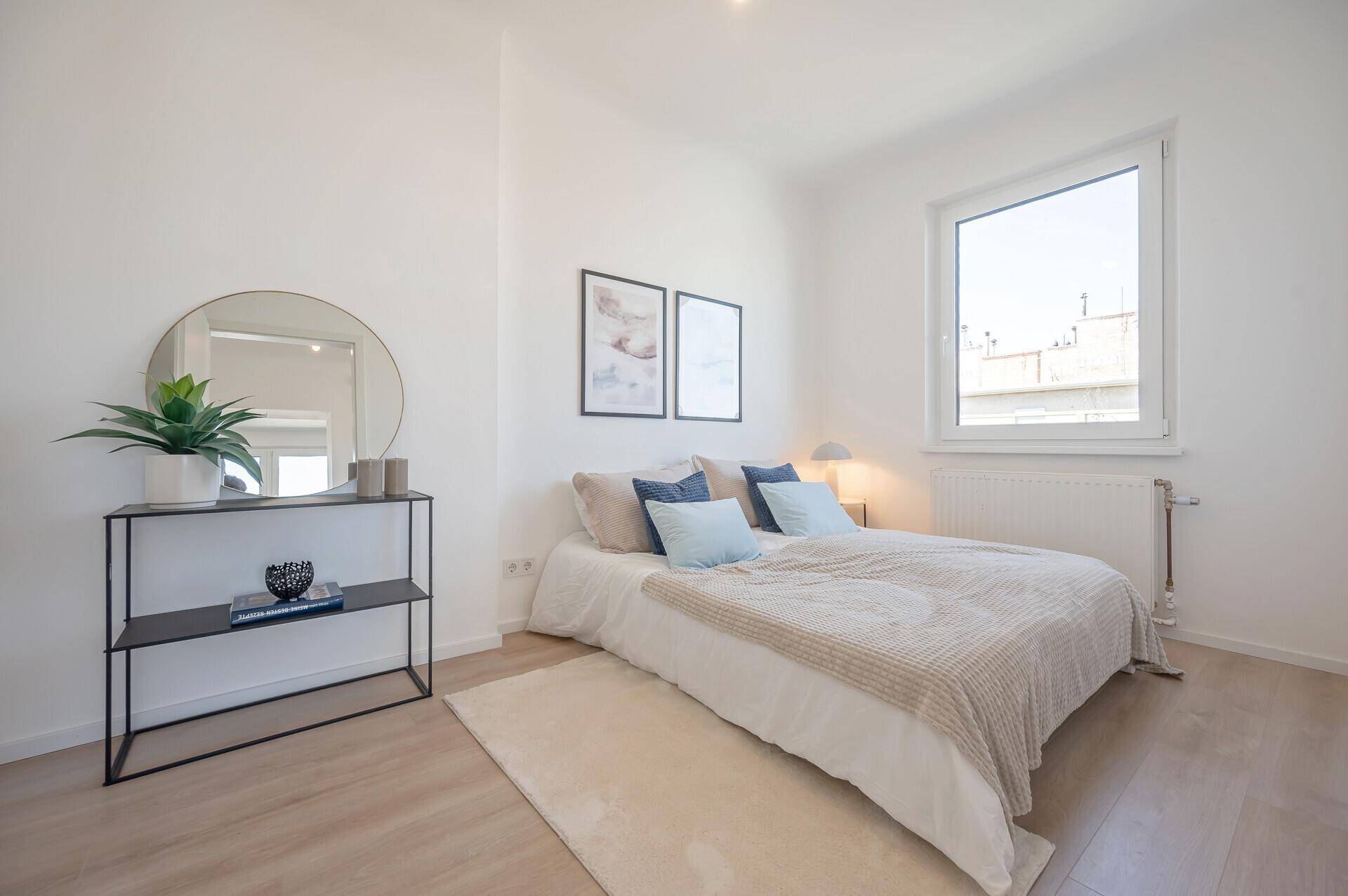 Schlafzimmer mit hellem Laminatboden, großem Fenster und modernem Spiegel.