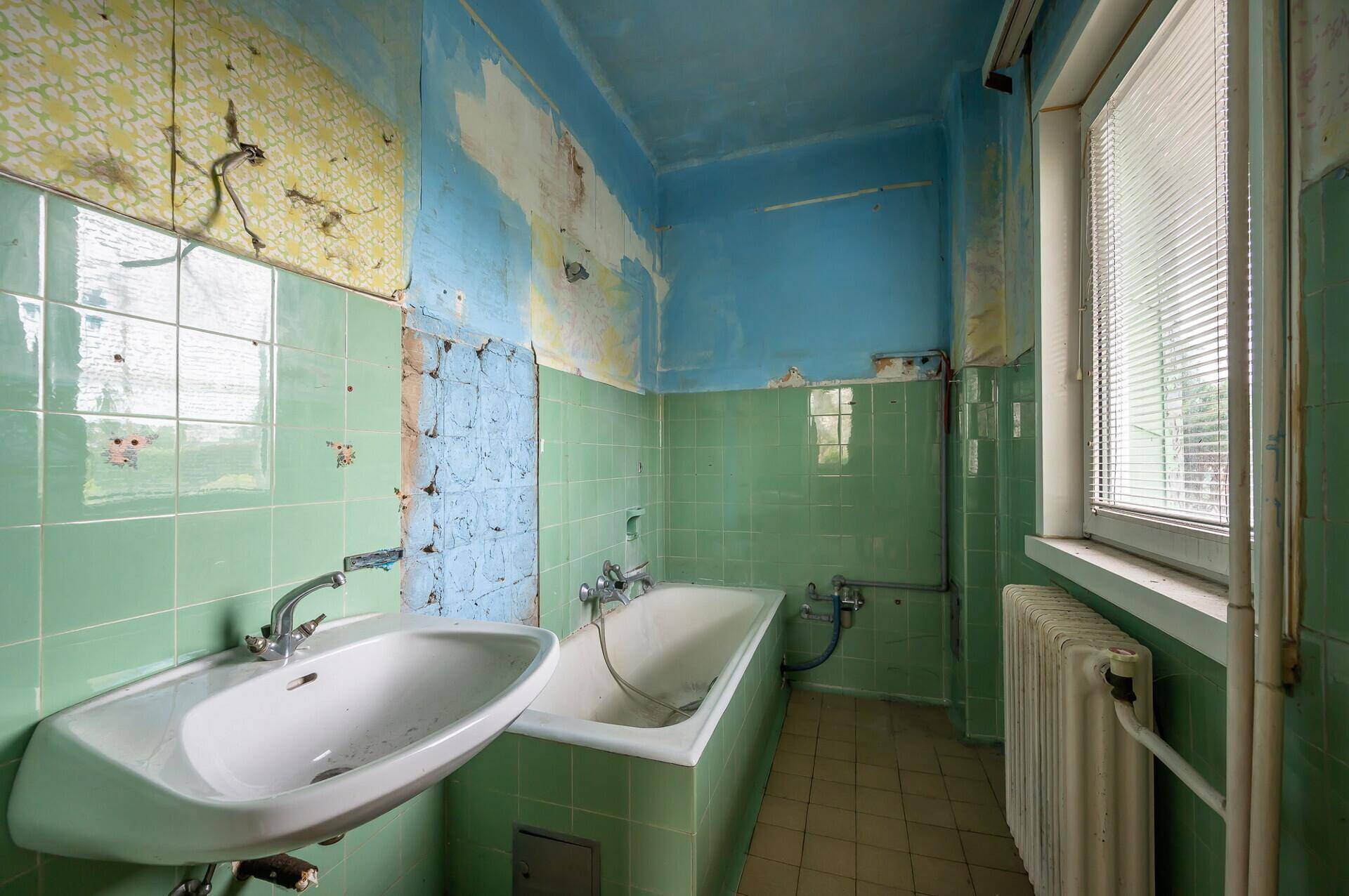 Badezimmer mit grünen Fliesen, Badewanne, Waschbecken und Fenster, sanierungsbedürftig.