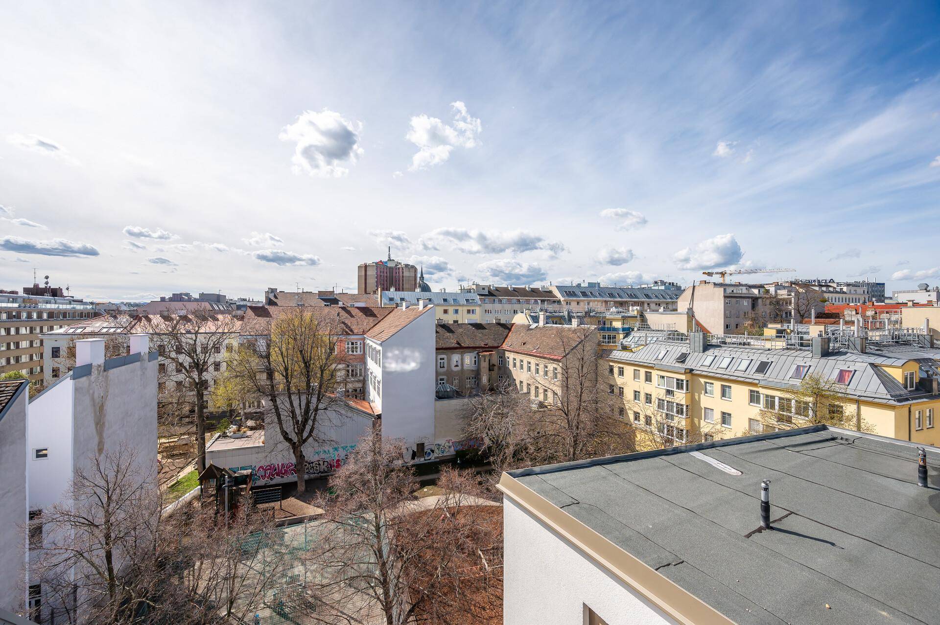 Weitläufiger Blick über die Dächer der Stadt mit Bäumen und urbaner Architektur.