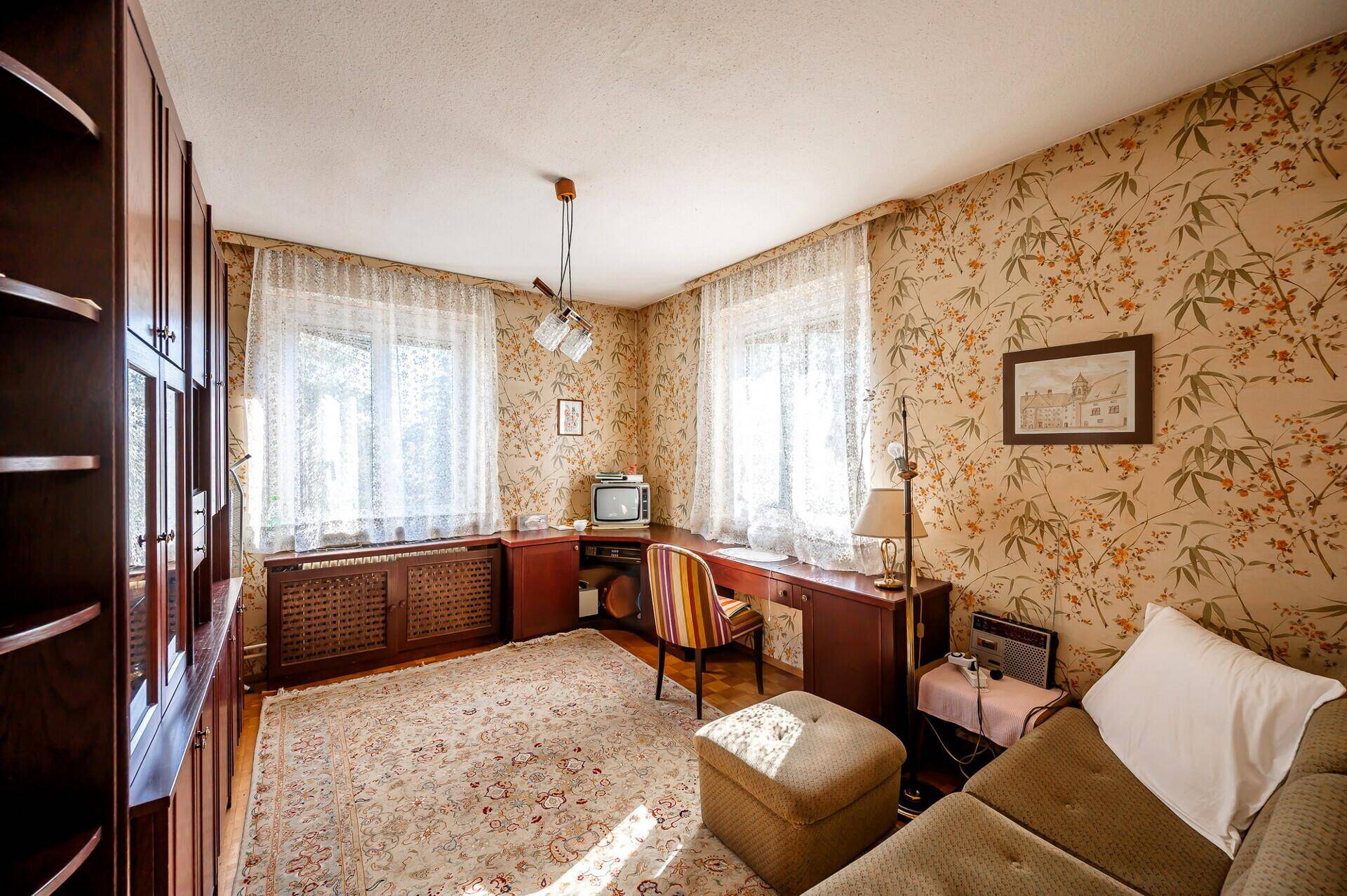 Arbeitszimmer mit floraler Tapete, Holzschreibtisch und traditionellem Teppich, hell und gemütlich.