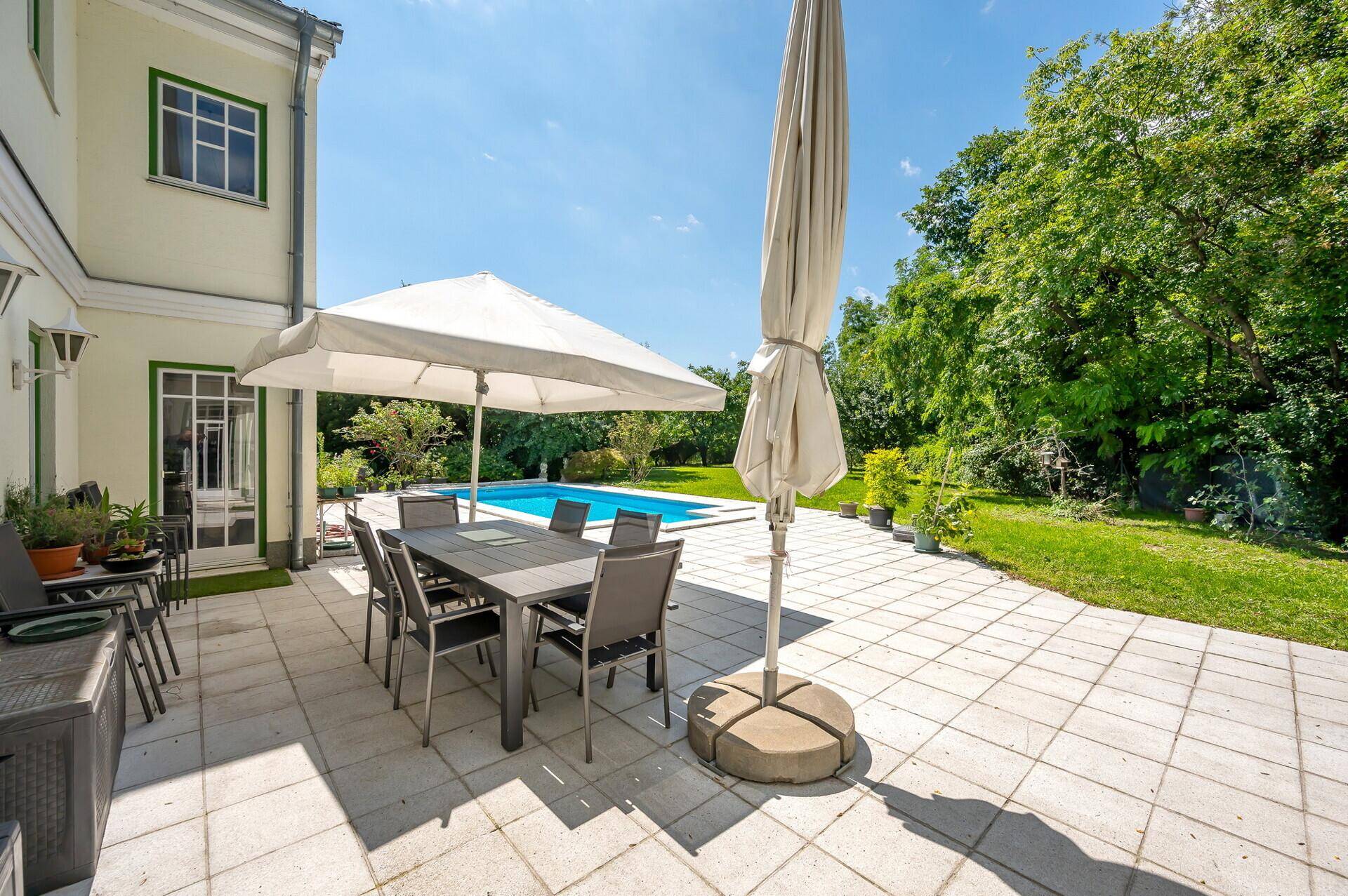 Große Sonnenterrasse mit Esstisch, Sonnenschirm und Blick auf den Pool.