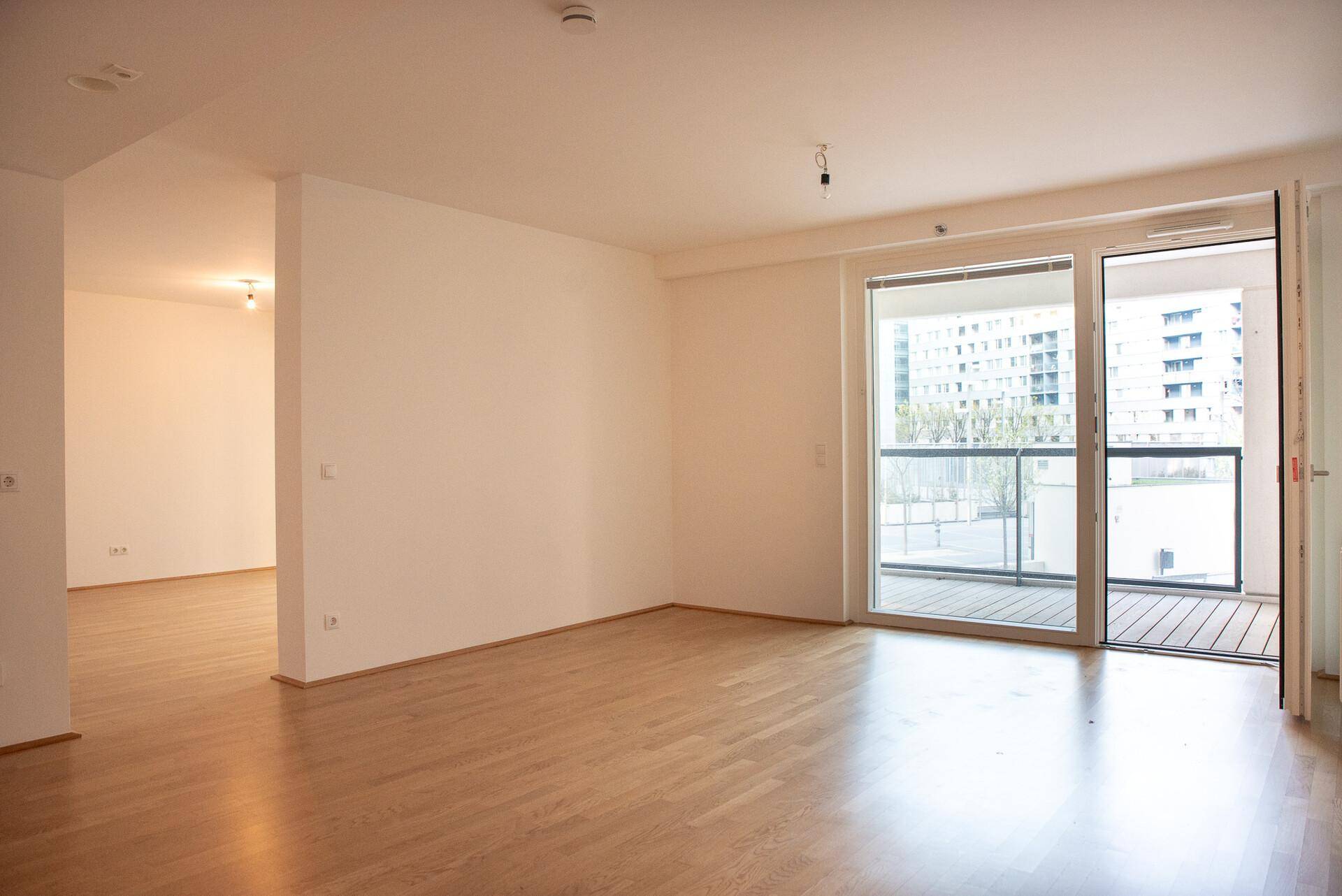 Heller, leerer Wohnbereich mit Holzboden und Zugang zu einem Balkon, ideal für individuelle Gestaltung.