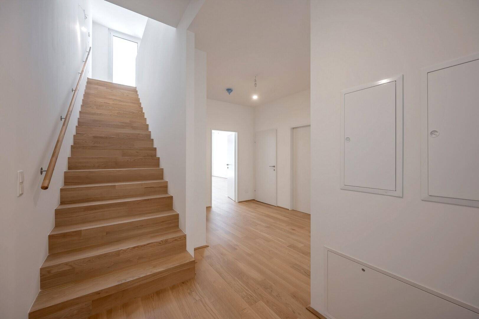 Heller Eingangsbereich mit Holztreppe, die in die obere Etage führt.