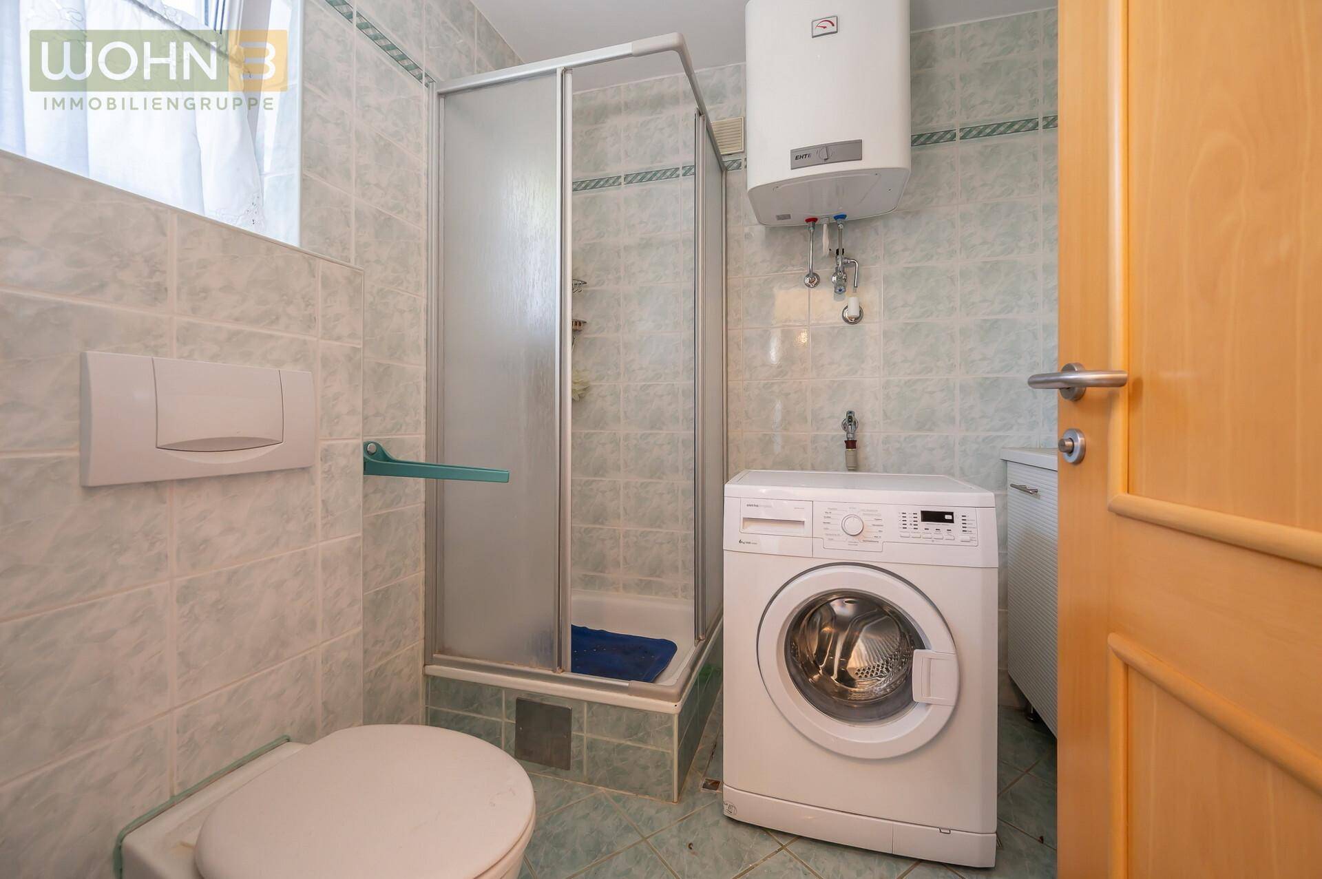 Badezimmer mit Duschkabine, Toilette und Waschmaschine, komplett gefliest in hellem Grün.