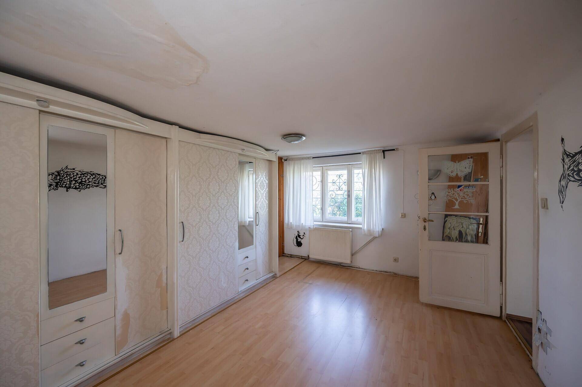 Schlafzimmer mit Laminatboden, großem Fenster und Einbauschränken, renovierungsbedürftig.
