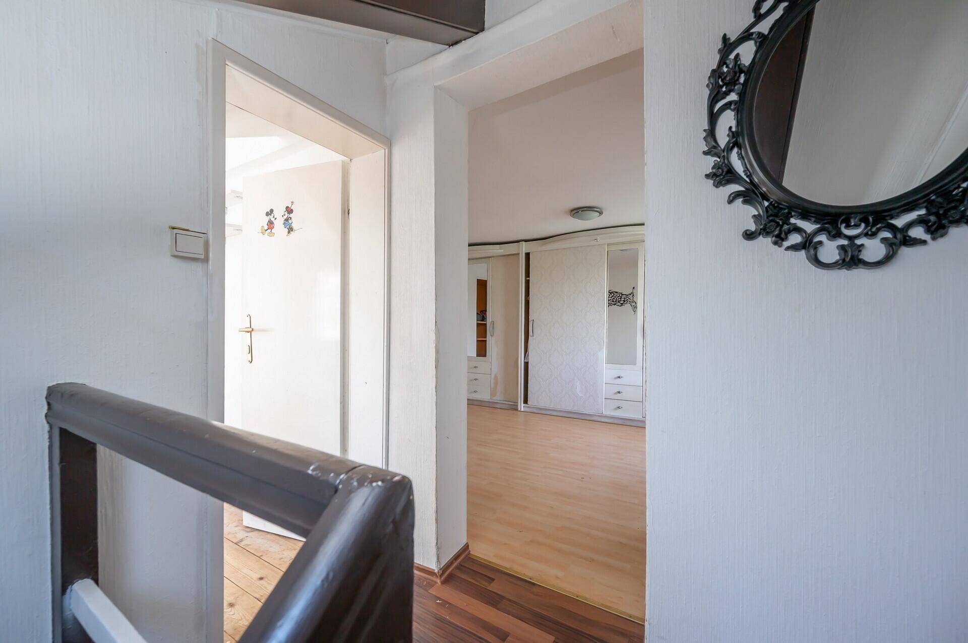 Treppenaufgang führt zu einem Zimmer mit Parkettboden und Spiegel, renovierungsbedürftig.