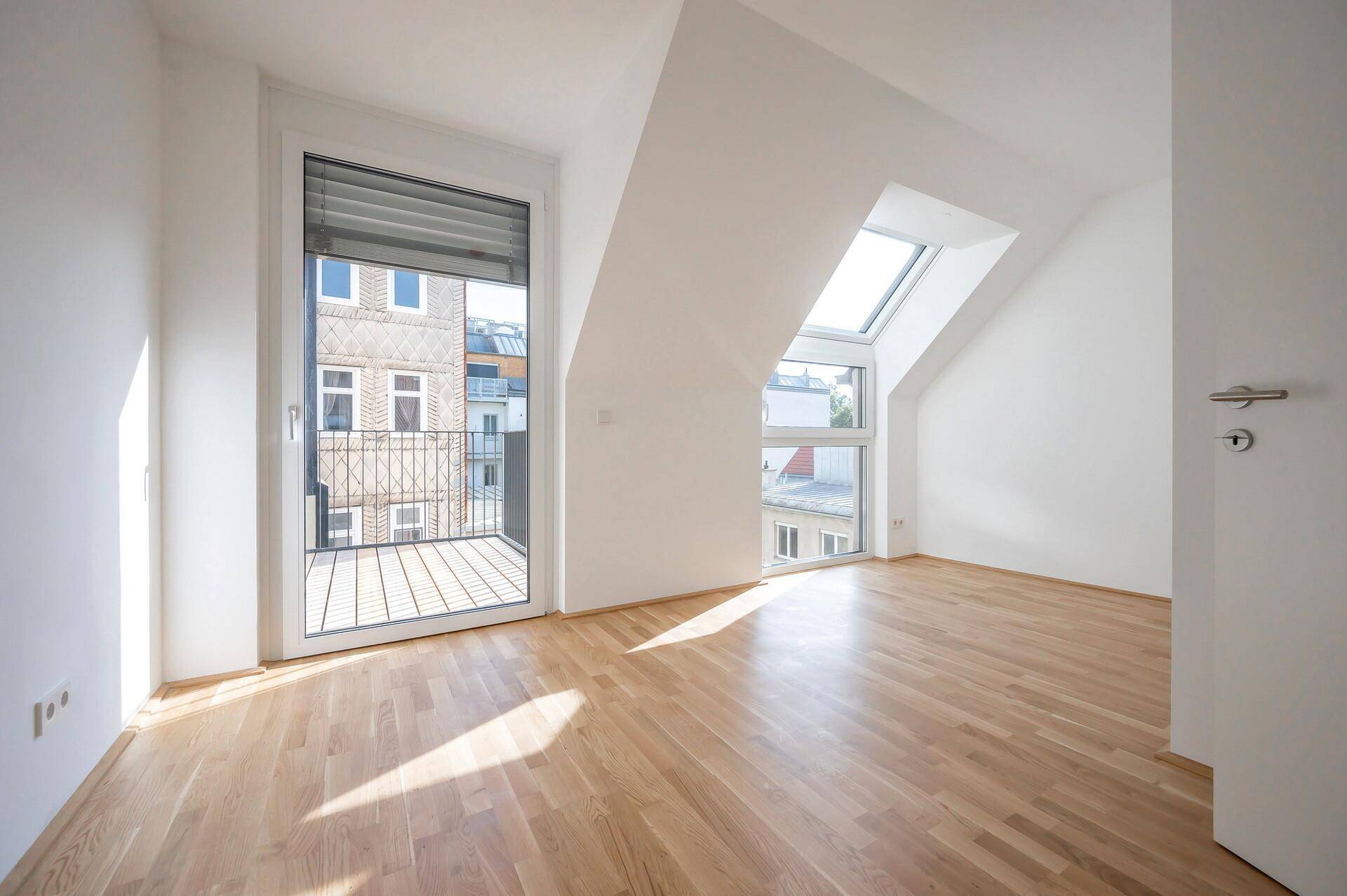 Helles Dachzimmer mit Parkettboden, Schrägdach und Zugang zu einem französischen Balkon.