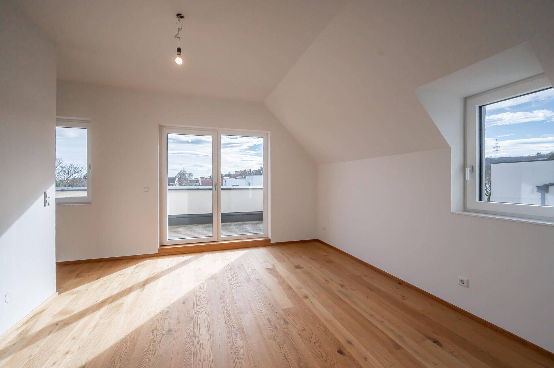 Helles Schlafzimmer im Dachgeschoss mit Holzboden und Zugang zur Dachterrasse.