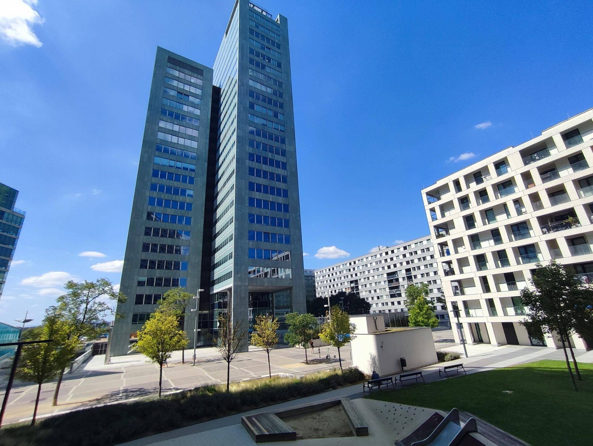 Moderne Hochhäuser und Wohngebäude unter blauem Himmel, umgeben von Grünflächen.