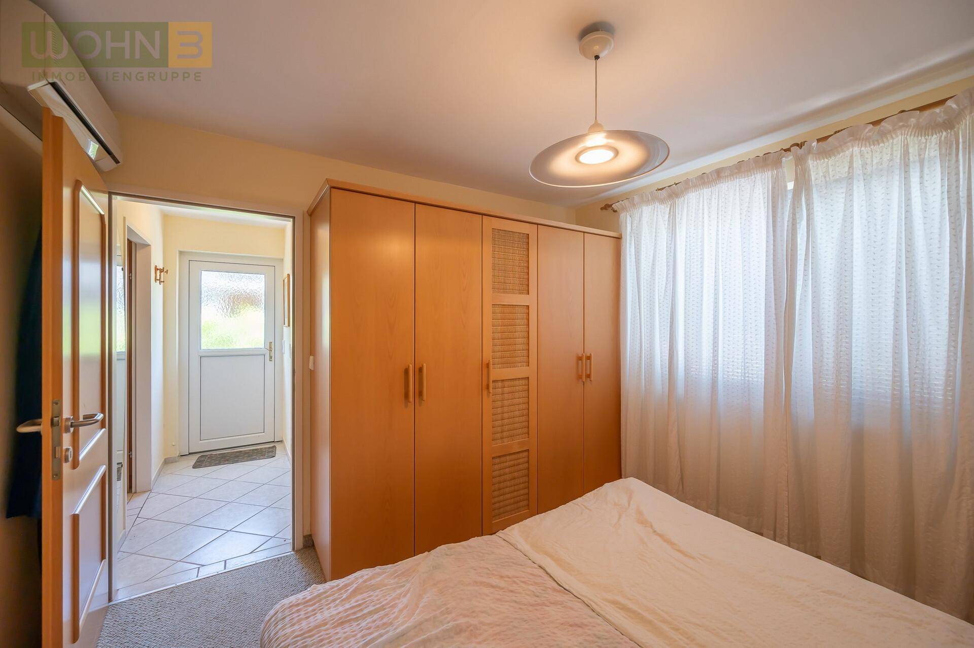 Schlafzimmer mit großem Holzschrank und Blick auf den Eingangsbereich mit Fliesenboden.