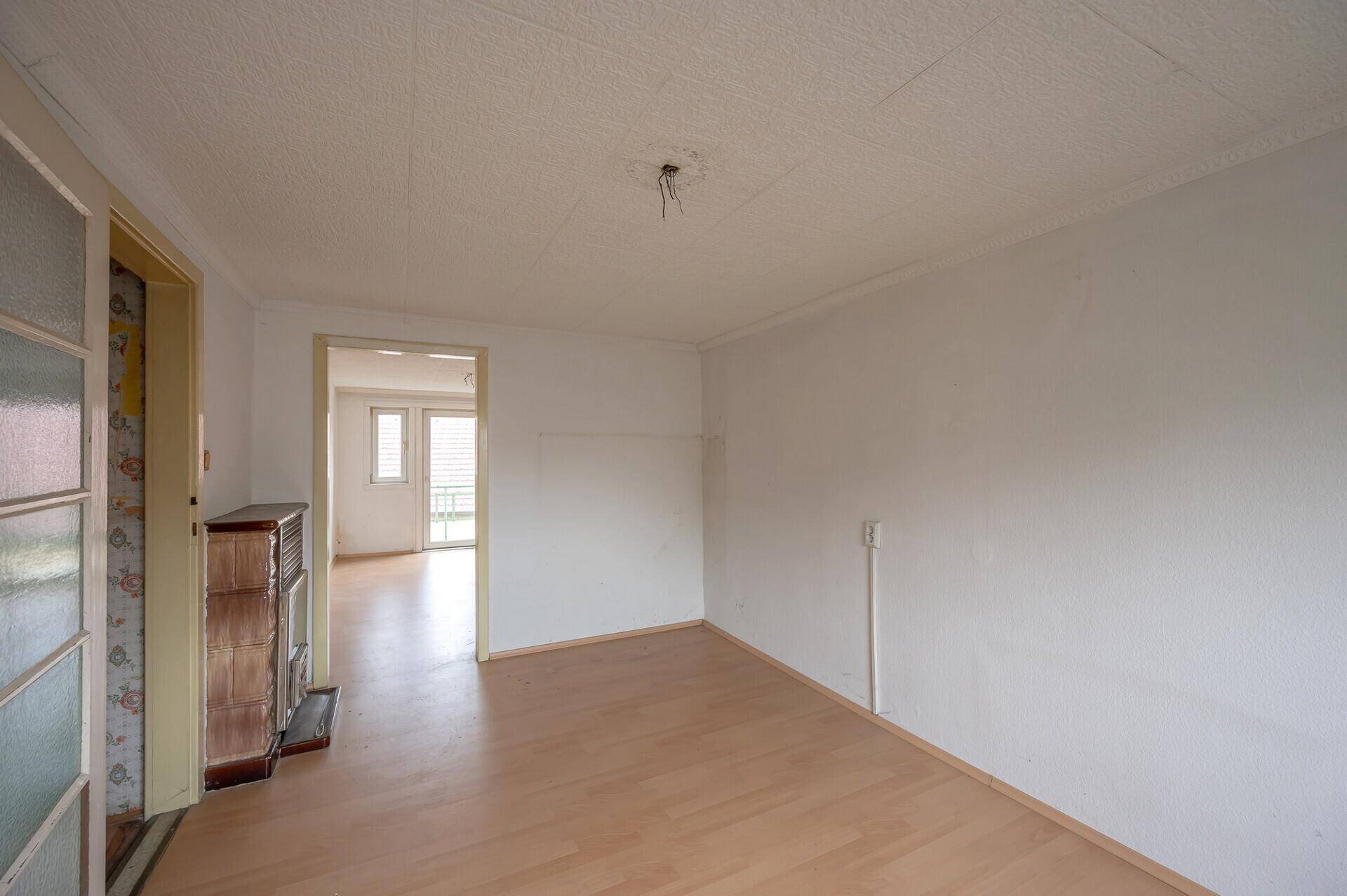 Geräumiger Wohnraum mit Holzboden und Kachelofen, bereit zur individuellen Gestaltung.