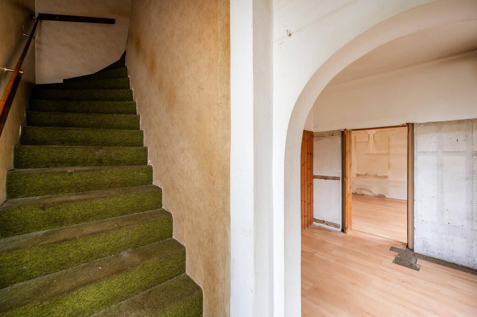 Treppenhaus mit grünem Teppichboden und Rundbogen, der zu den Wohnbereichen führt.