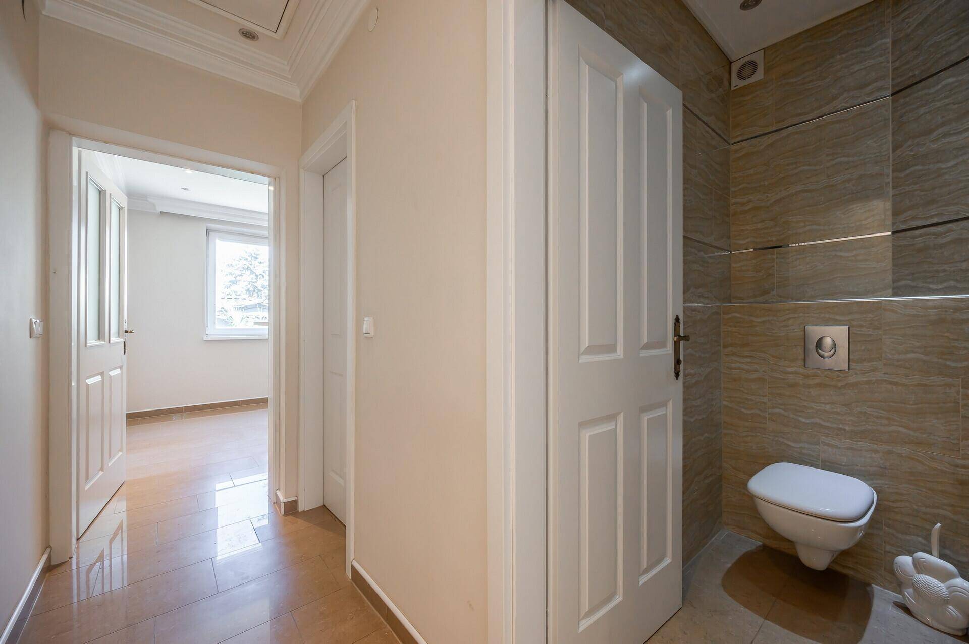 Flur mit Fliesenboden und Zugang zu einem modernen WC mit Wand-WC.
