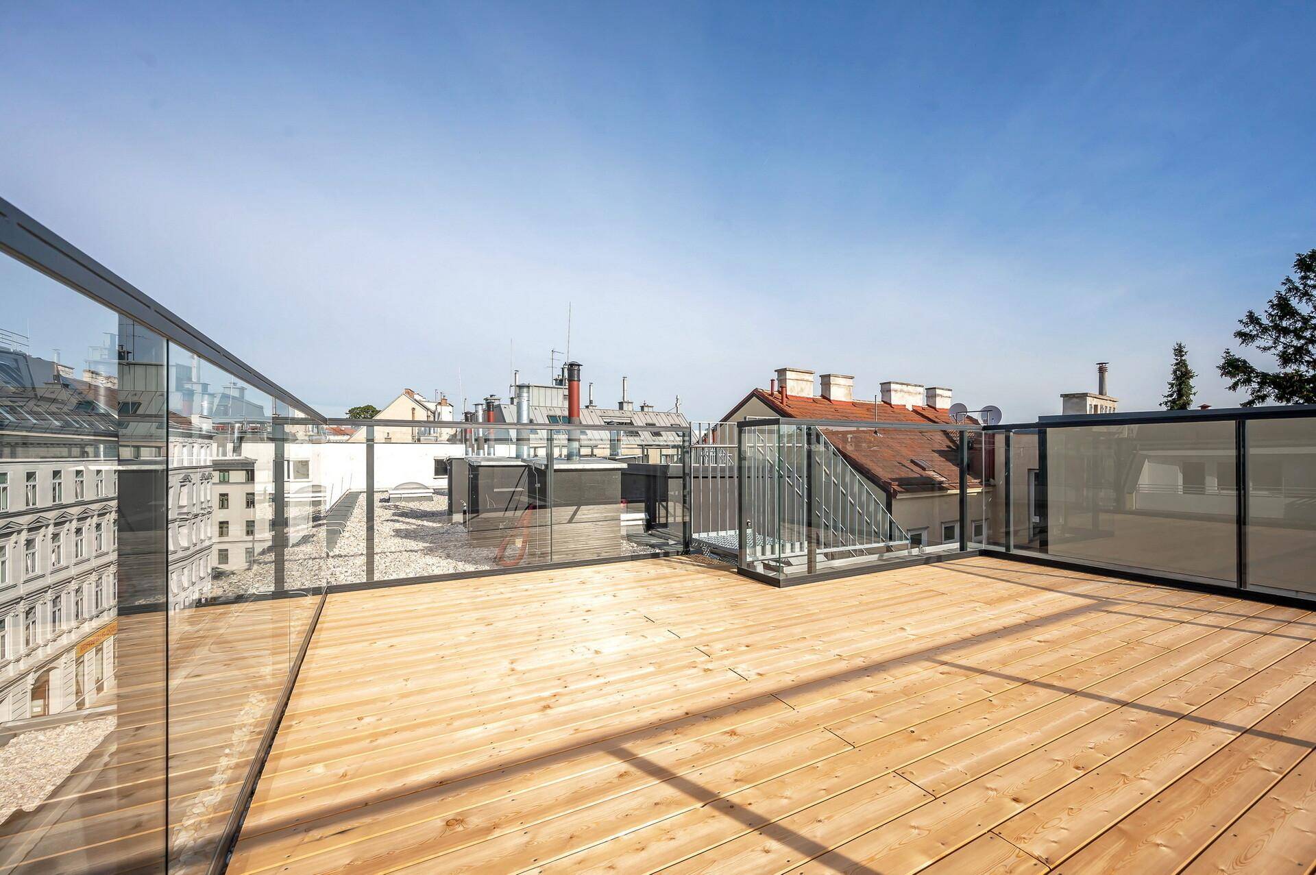 Geräumige Dachterrasse mit Holzboden und moderner Glasbrüstung, ideal für Entspannung im Freien.