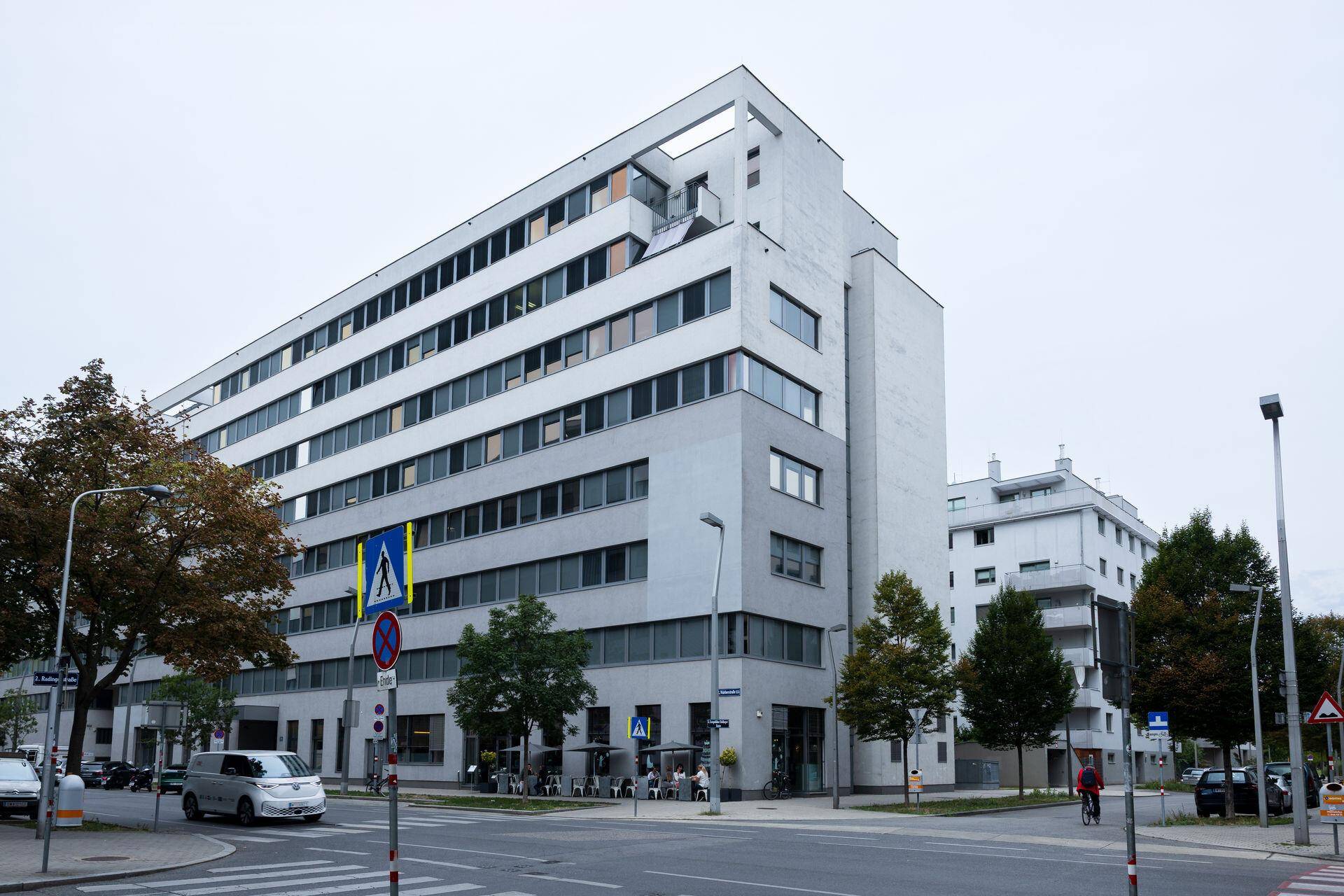 Modernes mehrstöckiges Gebäude an einer Straßenecke unter bewölktem Himmel.