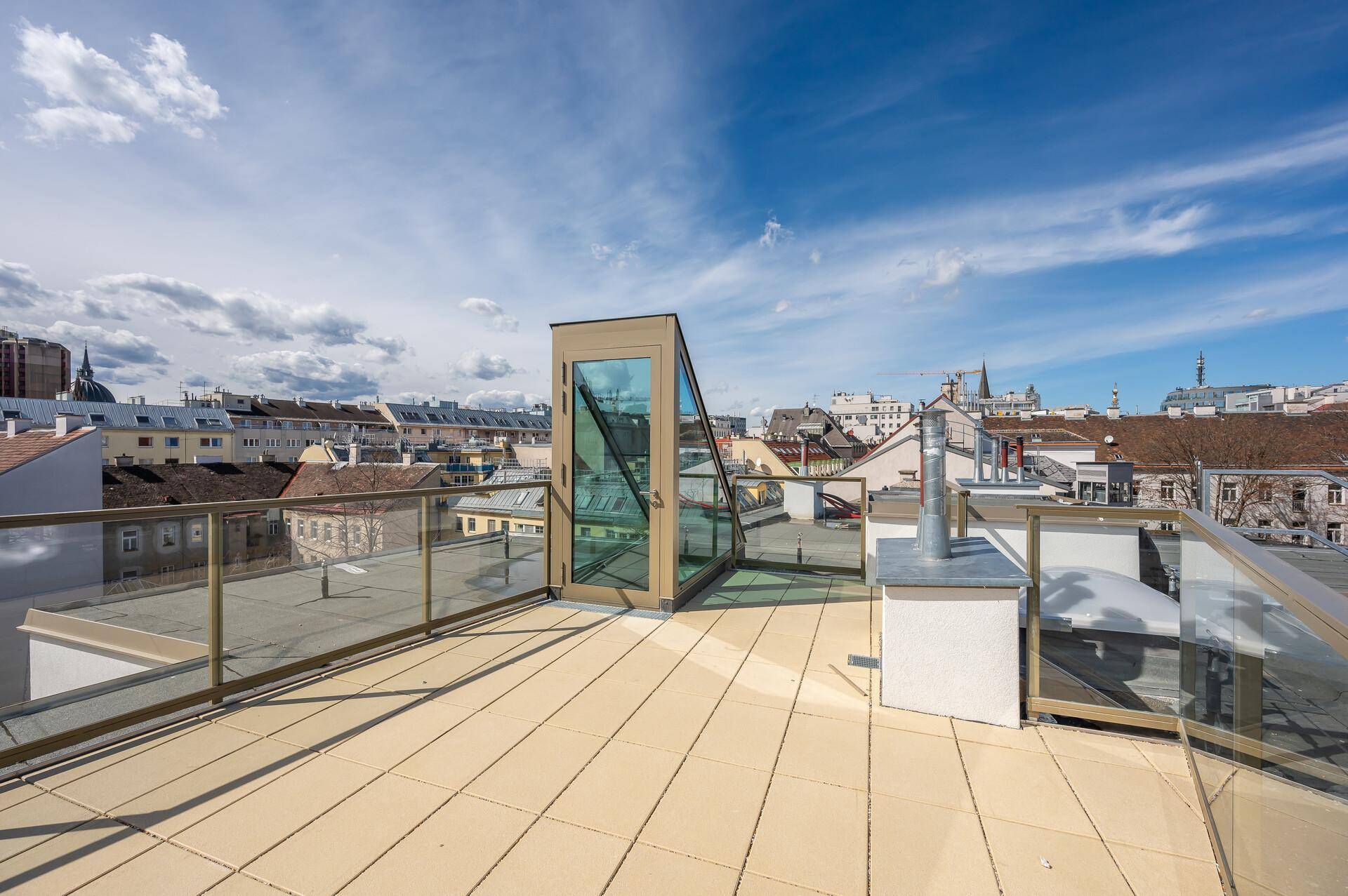 Geräumige Dachterrasse mit Fliesenboden, Glasgeländer und Panoramablick über die Stadt.