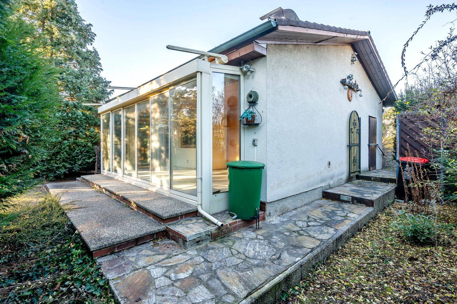 Anbau mit Wintergarten und großen Glasflächen, umgeben von einer gepflasterten Terrasse.