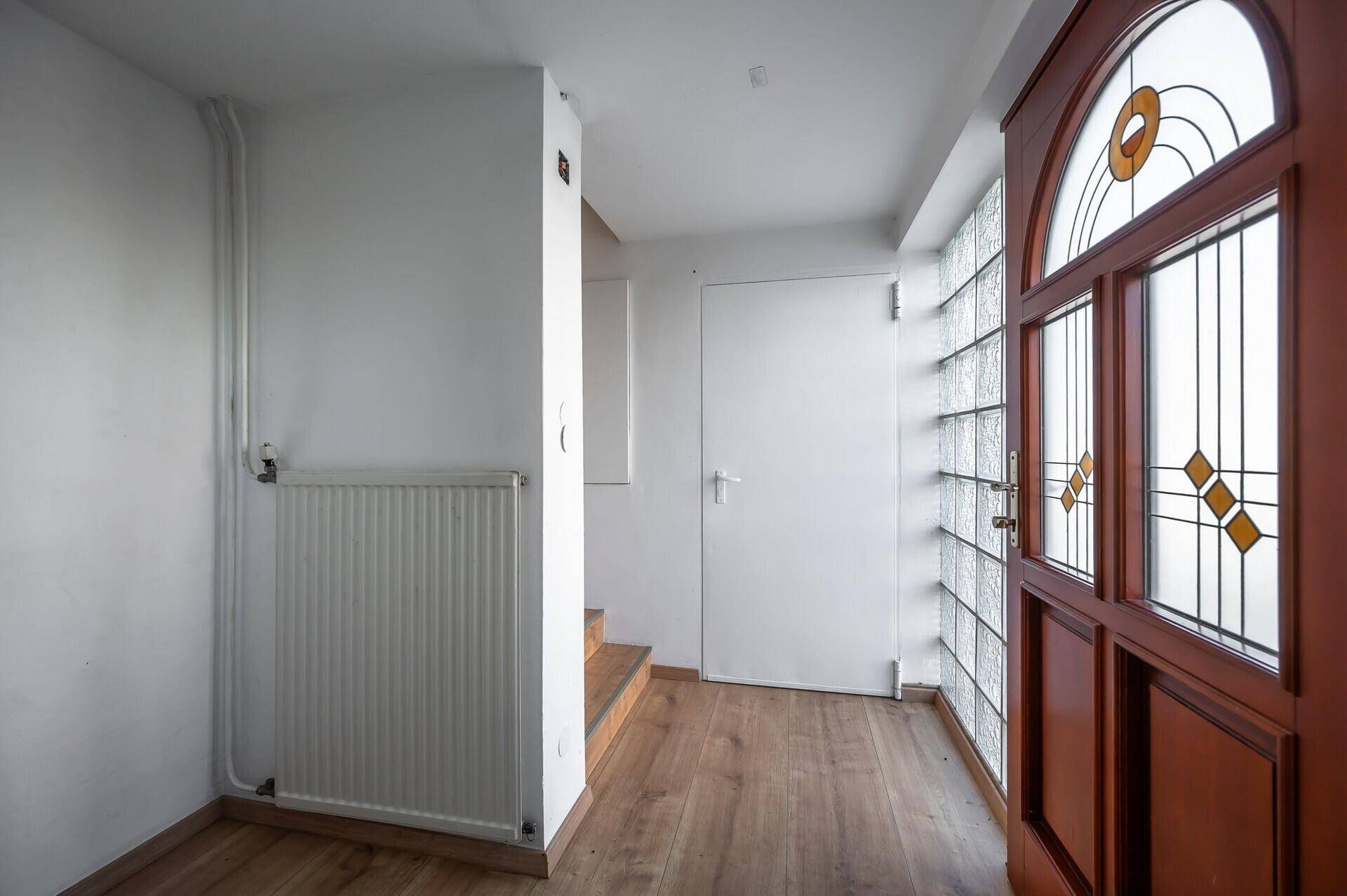 Heller Eingangsbereich mit Holzboden, Heizkörper und einer verzierten Eingangstür mit Buntglas.