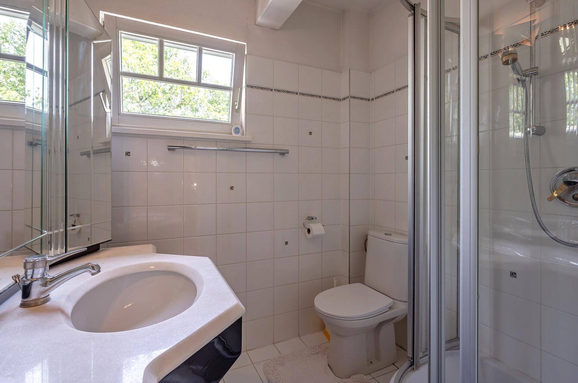 Helles Badezimmer mit Dusche, Waschbecken und Fenster.