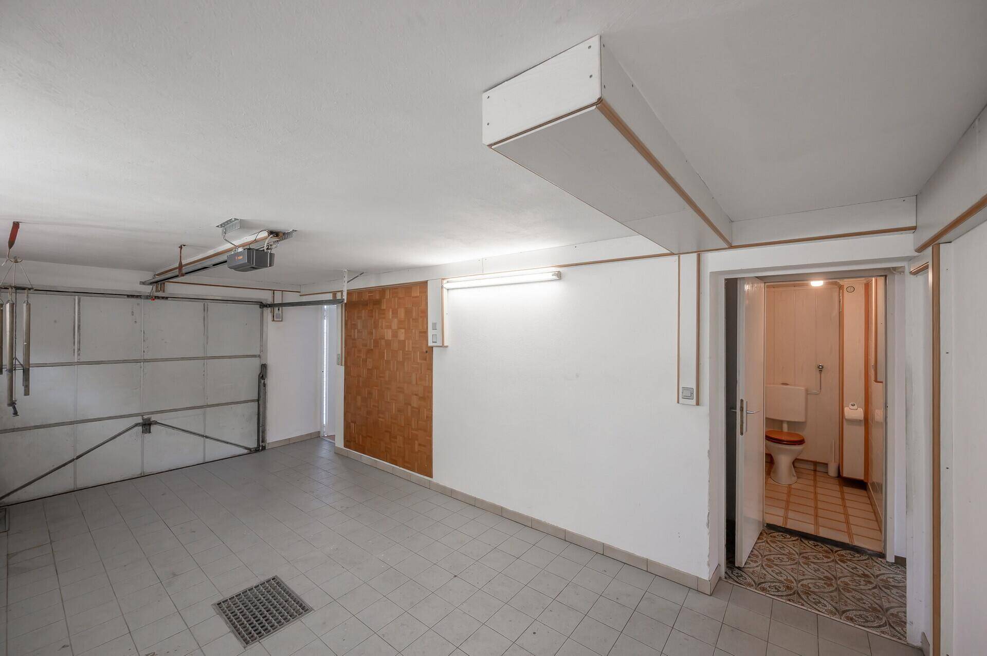 Garage mit Fliesenboden und Zugang zu einer separaten Toilette, ideal für Werkstattnutzung.