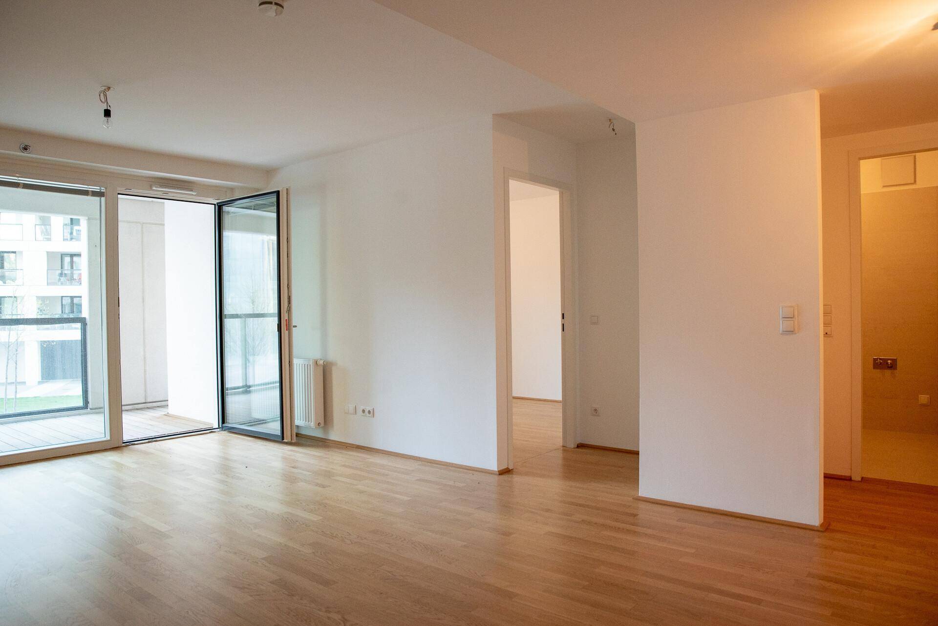 Geräumiger, heller Wohnbereich mit Holzboden, Heizkörper und Zugang zu einem Balkon.
