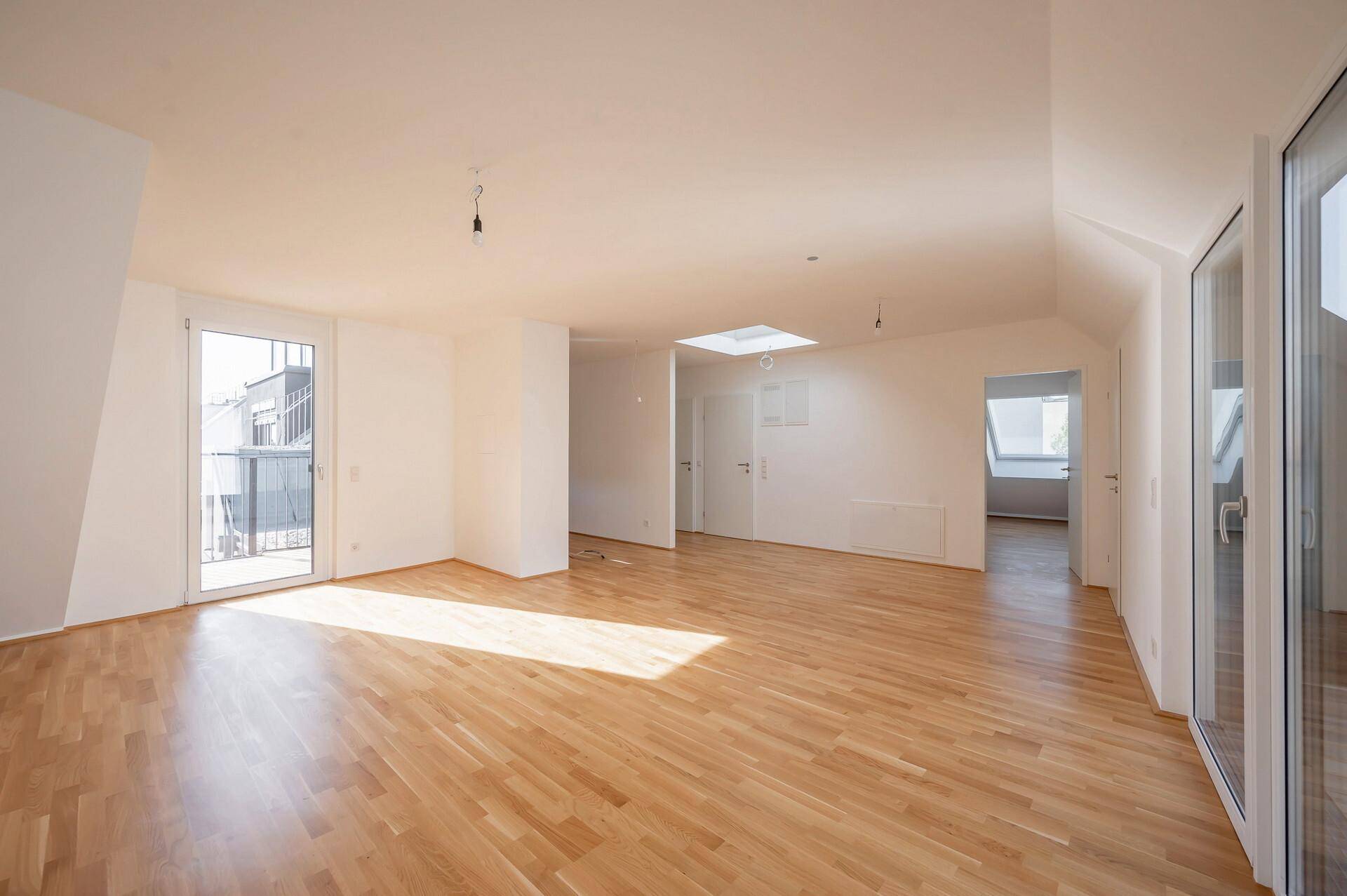 Heller Dachgeschoss-Wohnraum mit Parkettboden, Dachfenster und Zugang zu einem Außenbereich.