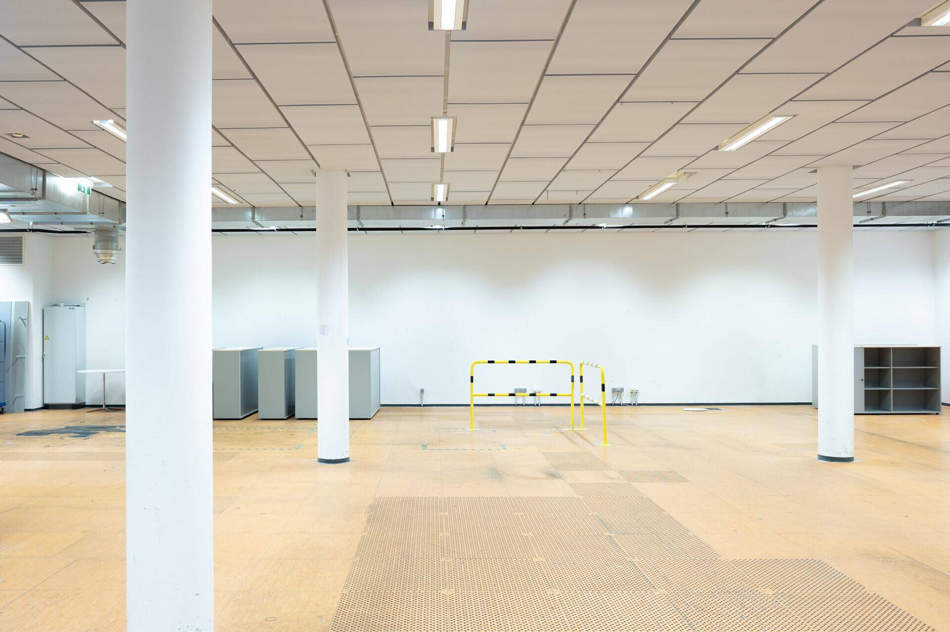 Großer, offener Gewerberaum mit mehreren tragenden Säulen, funktionaler Beleuchtung und einem gelben Absperrbügel.