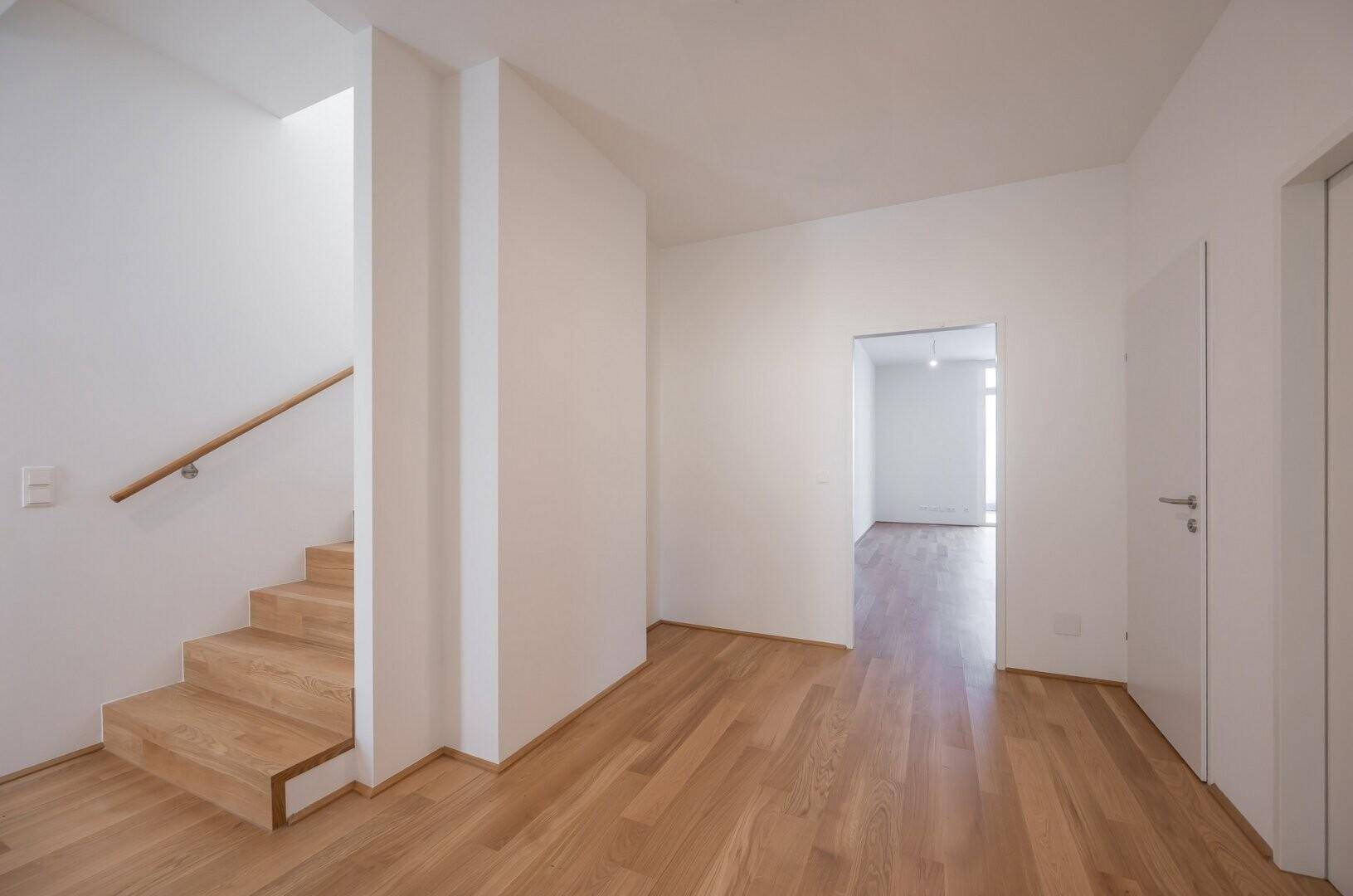 Heller Flur mit Holztreppe und Zugang zu weiteren Räumen im Erdgeschoss.