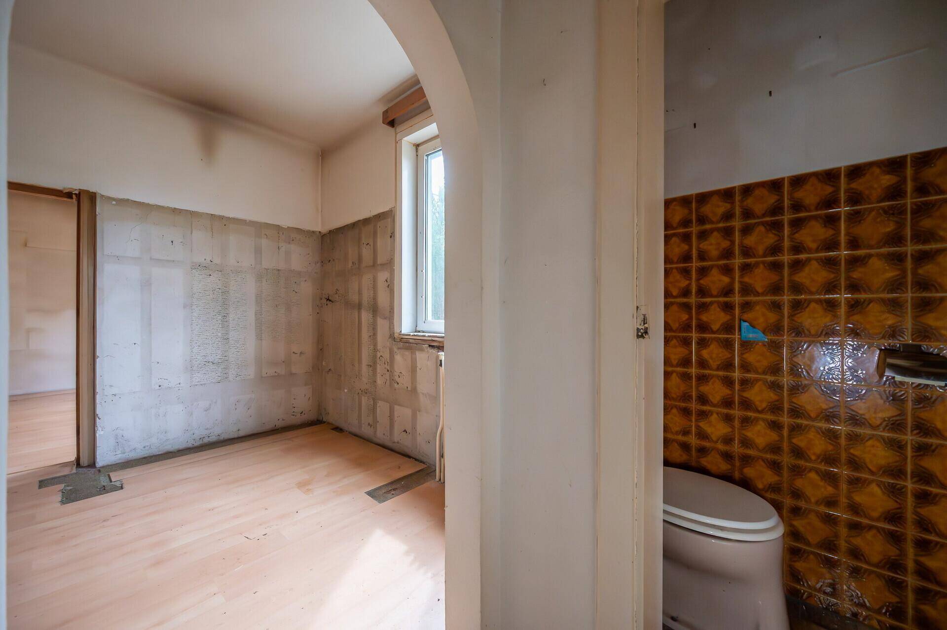 Kleines WC mit alten braunen Fliesen und Fenster, bereit zur Renovierung.