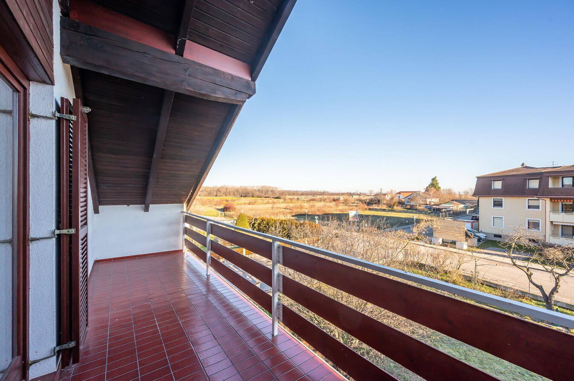 Großer Balkon mit roten Fliesen und weitem Blick über die Landschaft und umliegende Häuser.