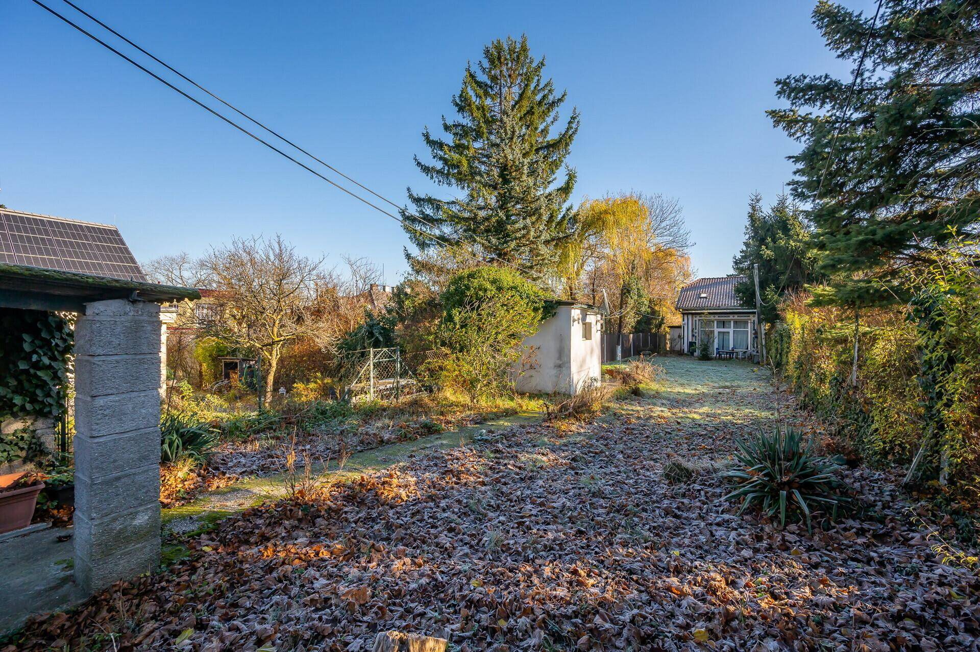 Großer Gartenbereich mit Rasenfläche, Bäumen und einem kleinen Schuppen unter klarem Himmel.