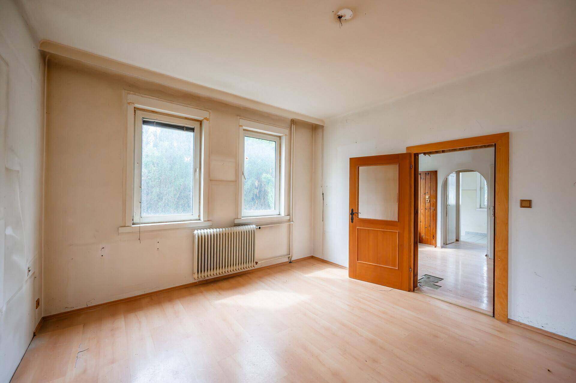 Wohnzimmer mit Holzboden und Holztür, die zu einem weiteren Raum führt.