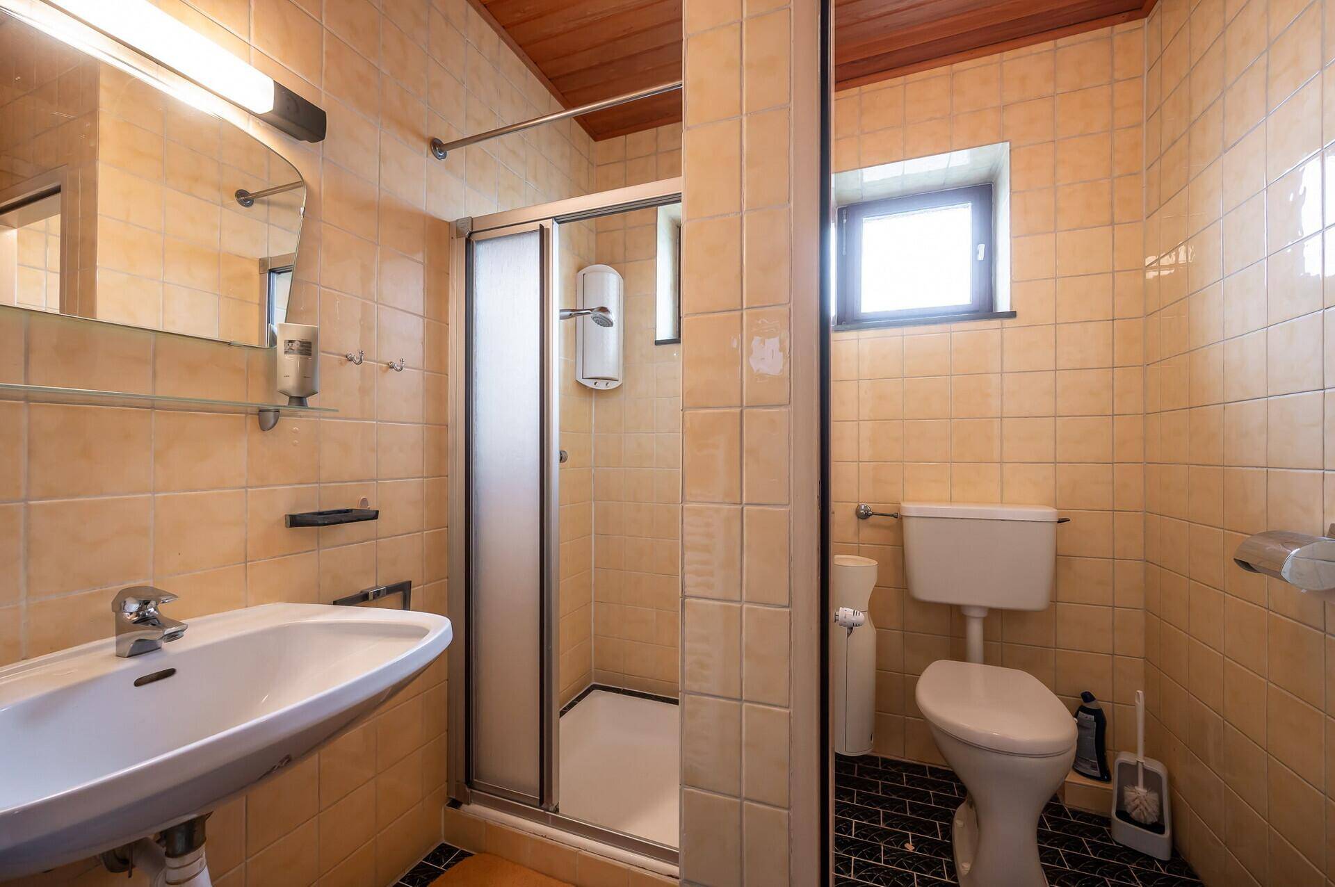 Badezimmer mit Duschkabine, Waschbecken und gelben Fliesen, ausgestattet mit einem Fenster.