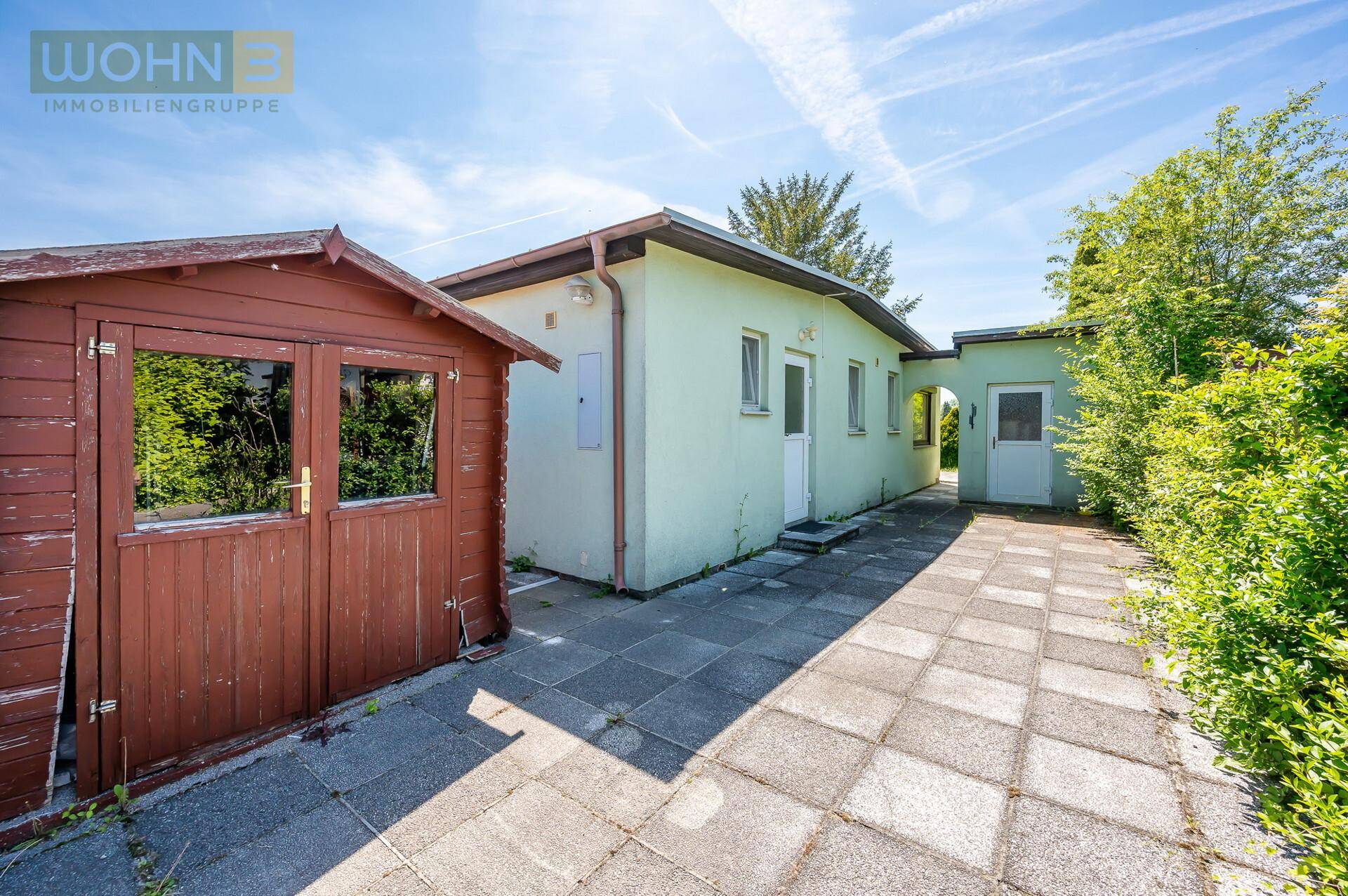 Rückseite des Hauses mit gepflastertem Weg, einem Holzschuppen und Anbau.