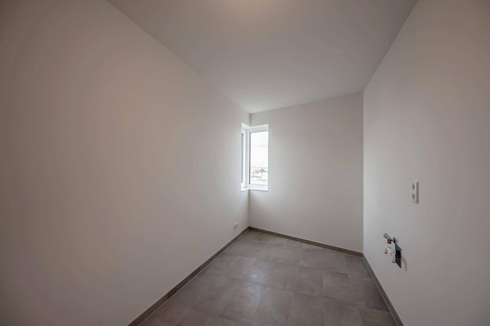 Kleiner Raum mit Fliesenboden und Fenster, ideal als Abstellraum nutzbar.